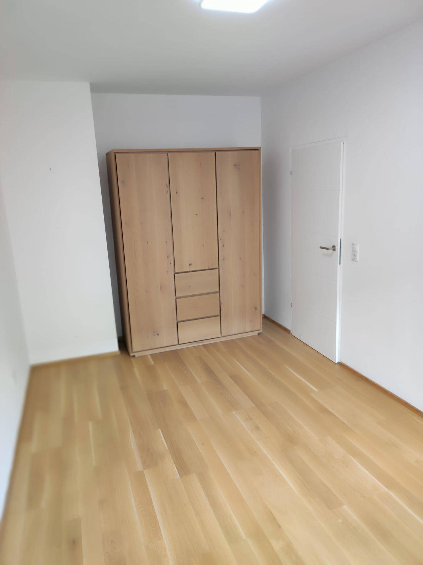Schlafzimmer mit hellem Parkettboden und einem modernen Holzschrank.