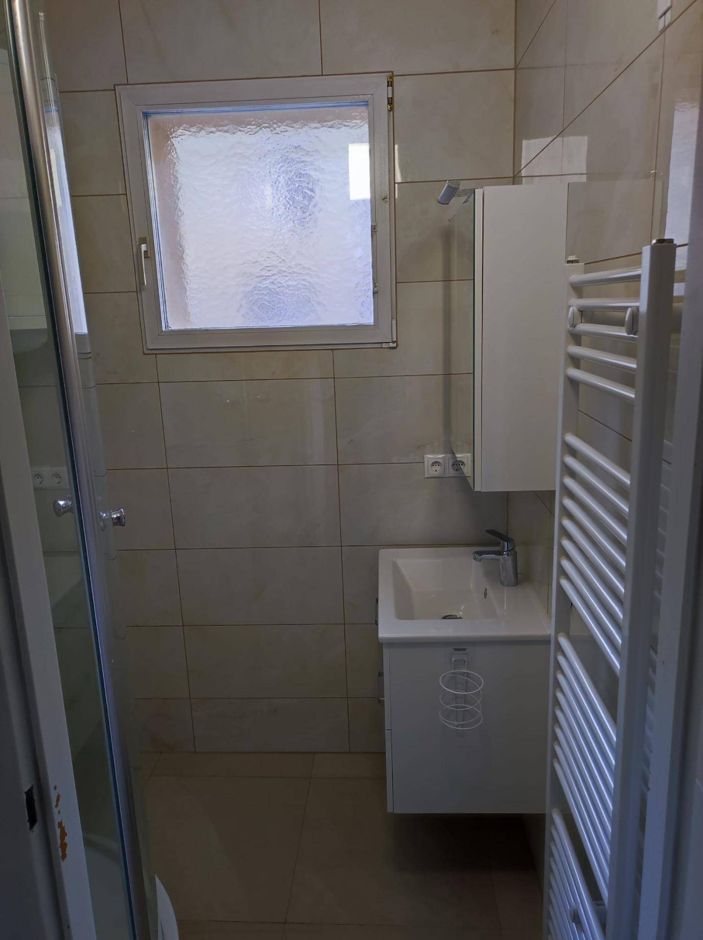 Modernes Badezimmer mit Duschkabine, Waschbecken, beheiztem Handtuchhalter und Fenster.