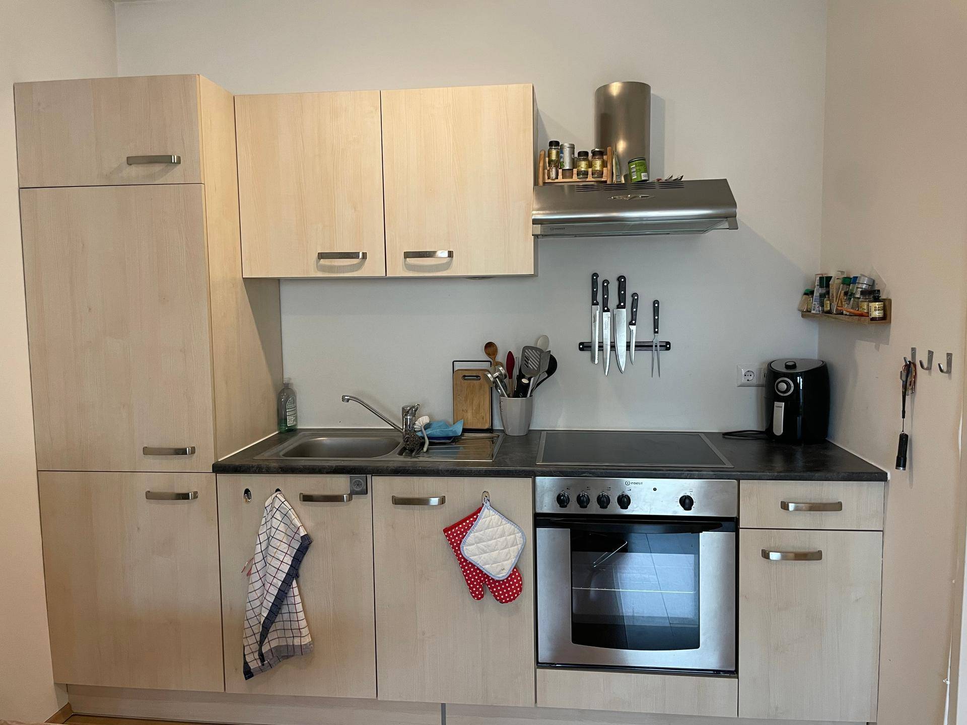 Kompakte Einbauküche mit hellen Holzschränken, dunkler Arbeitsplatte und modernen Geräten.
