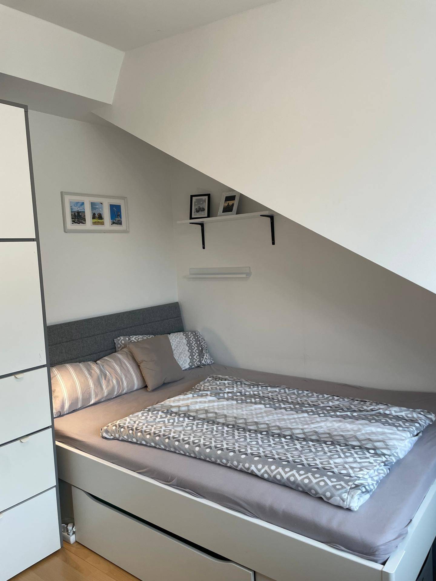 Gemütliches Schlafzimmer mit Bett, integrierten Schubladen und Dachschräge.