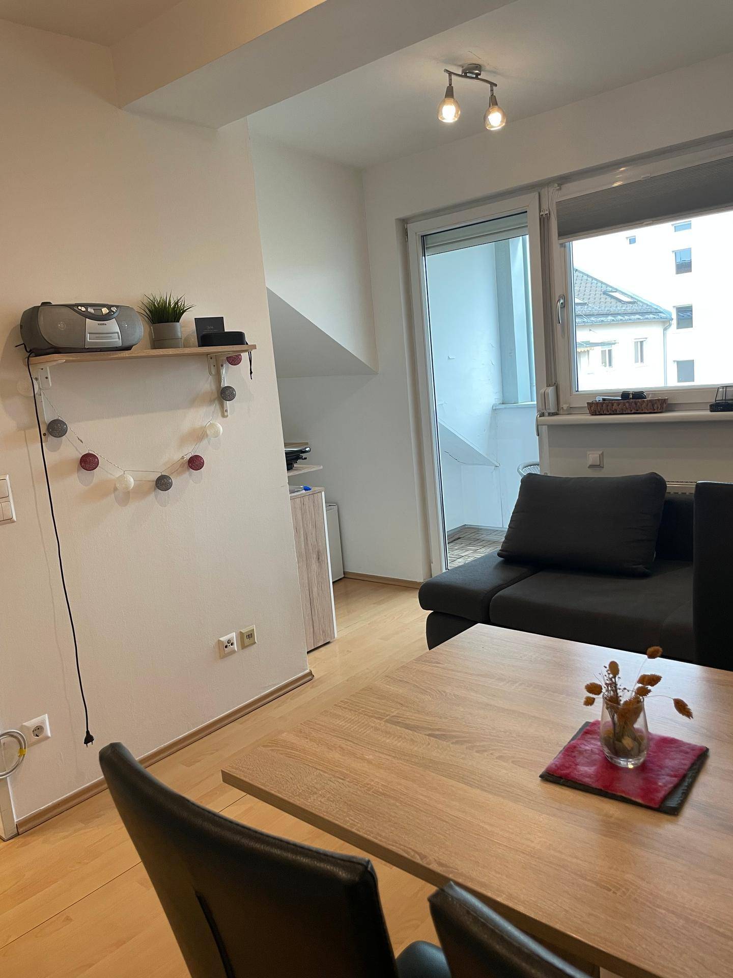 Wohnbereich mit Zugang zum Balkon, hellem Laminatboden und Dachschrägen.