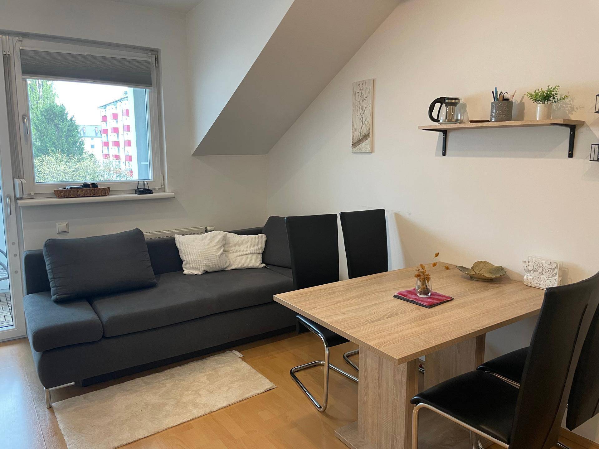 Heller Wohn- und Essbereich mit Sofa, Esstisch und Fenster in einem Dachgeschoss.