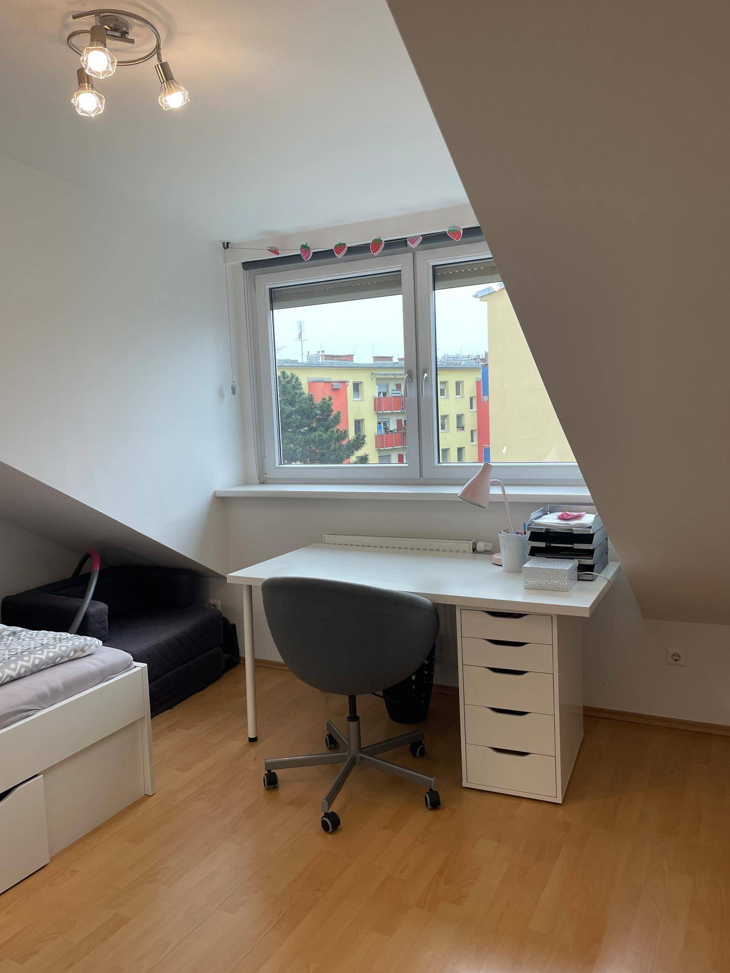 Helles Schlafzimmer mit Schreibtisch, Fenster und Dachschrägen, ideal als Arbeitsbereich.
