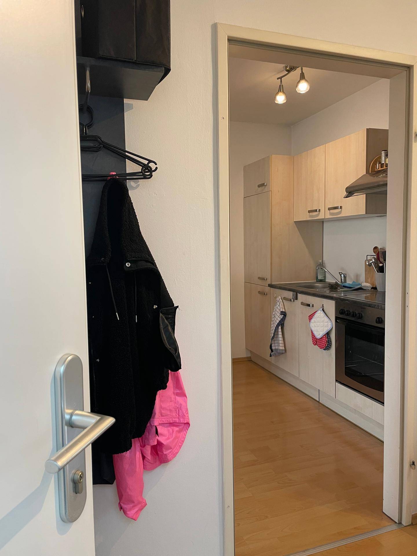Blick vom Flur in eine kleine, helle Küche mit Einbauschränken und Laminatboden.