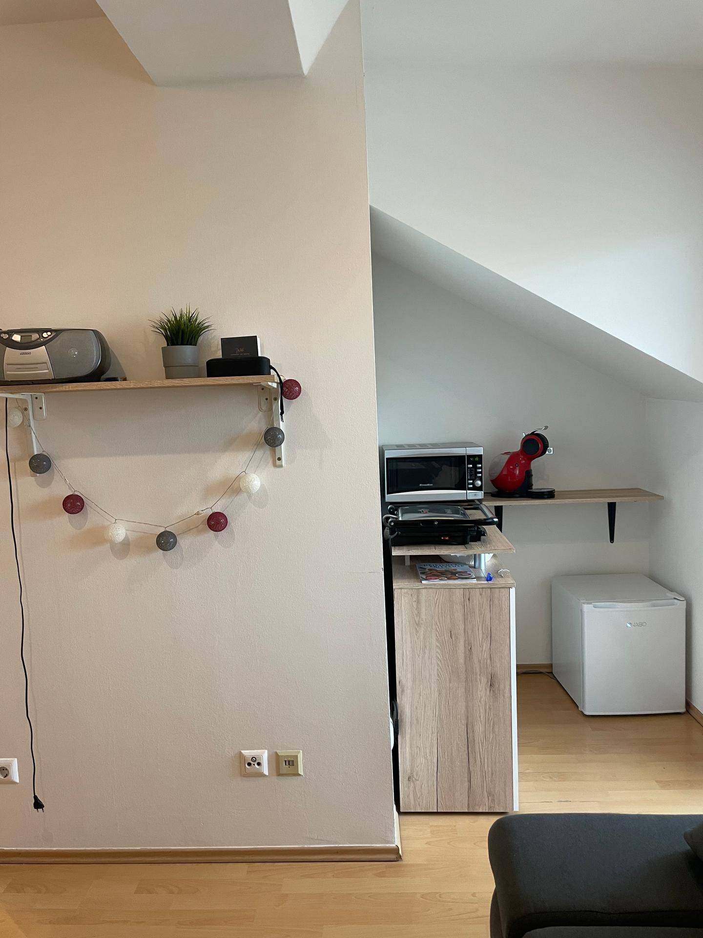 Wohnbereich mit Dachschräge, Regal und zusätzlichen Küchengeräten wie Mikrowelle.