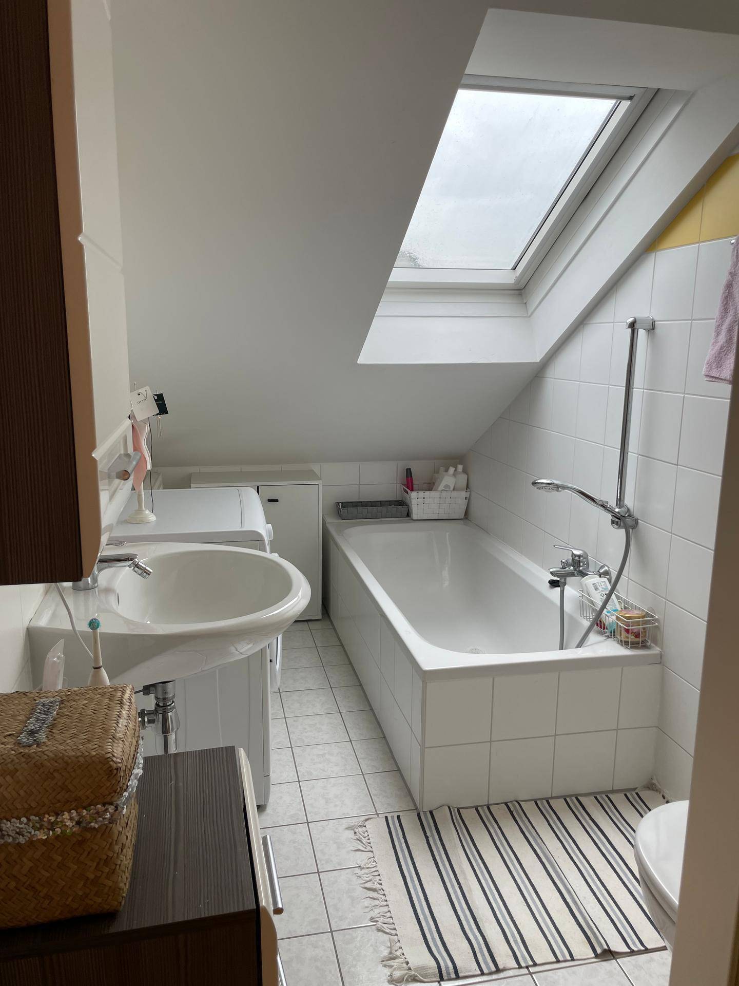 Helles Badezimmer mit Badewanne, Dachfenster und weißen Fliesen.
