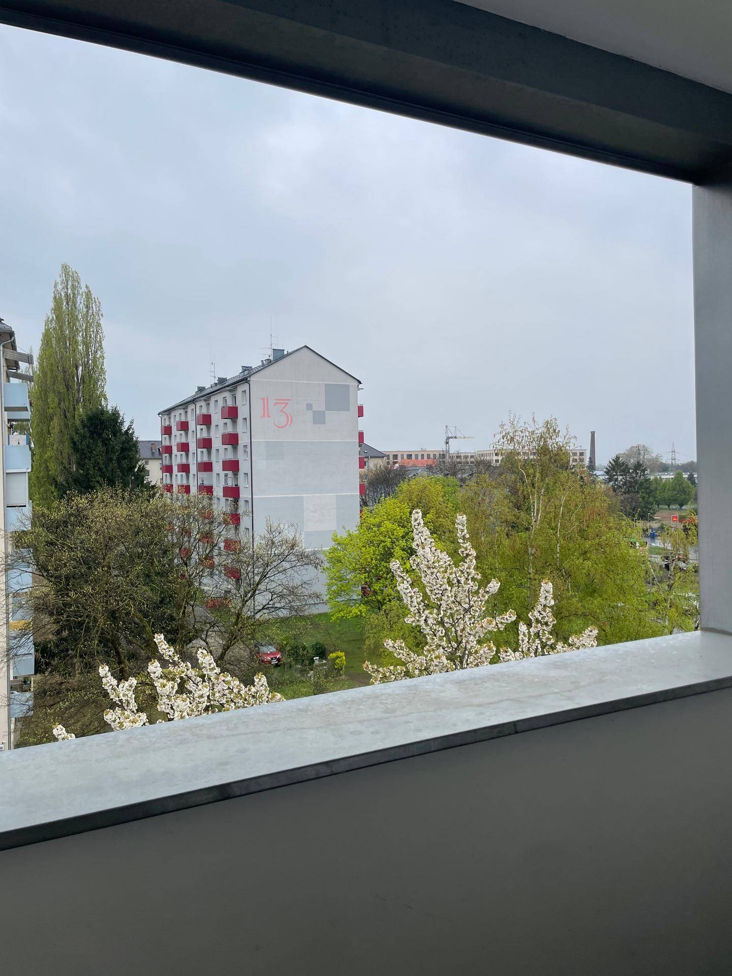 Ausblick vom Balkon auf umliegende Gebäude und grüne Bäume in der Nachbarschaft.