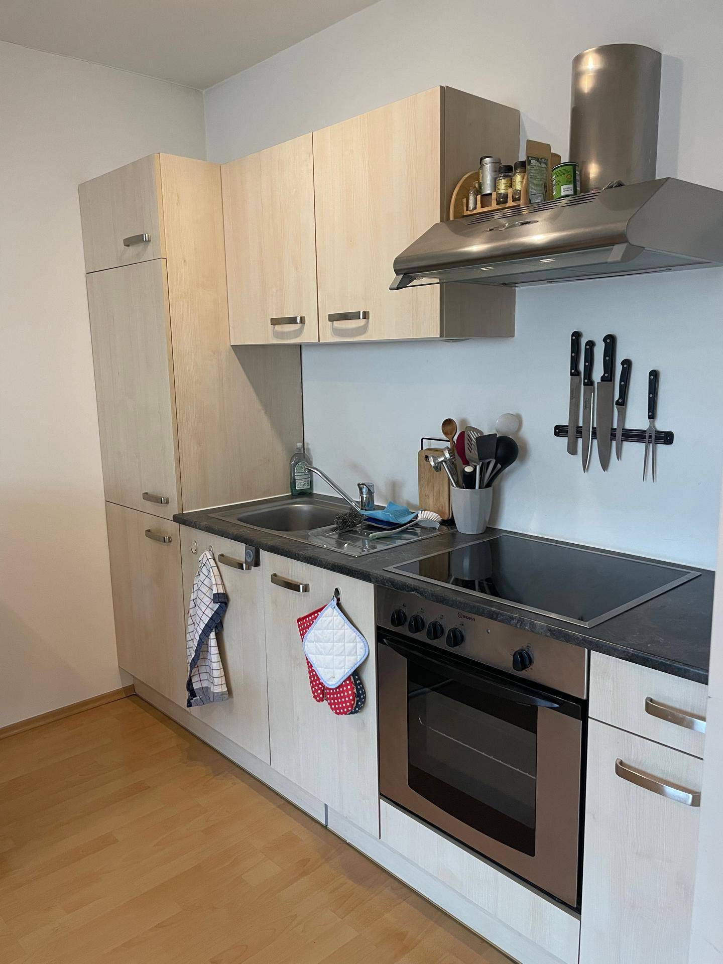 Funktionale Einbauküche mit hellen Holzfronten, dunkler Arbeitsplatte und modernen Geräten.