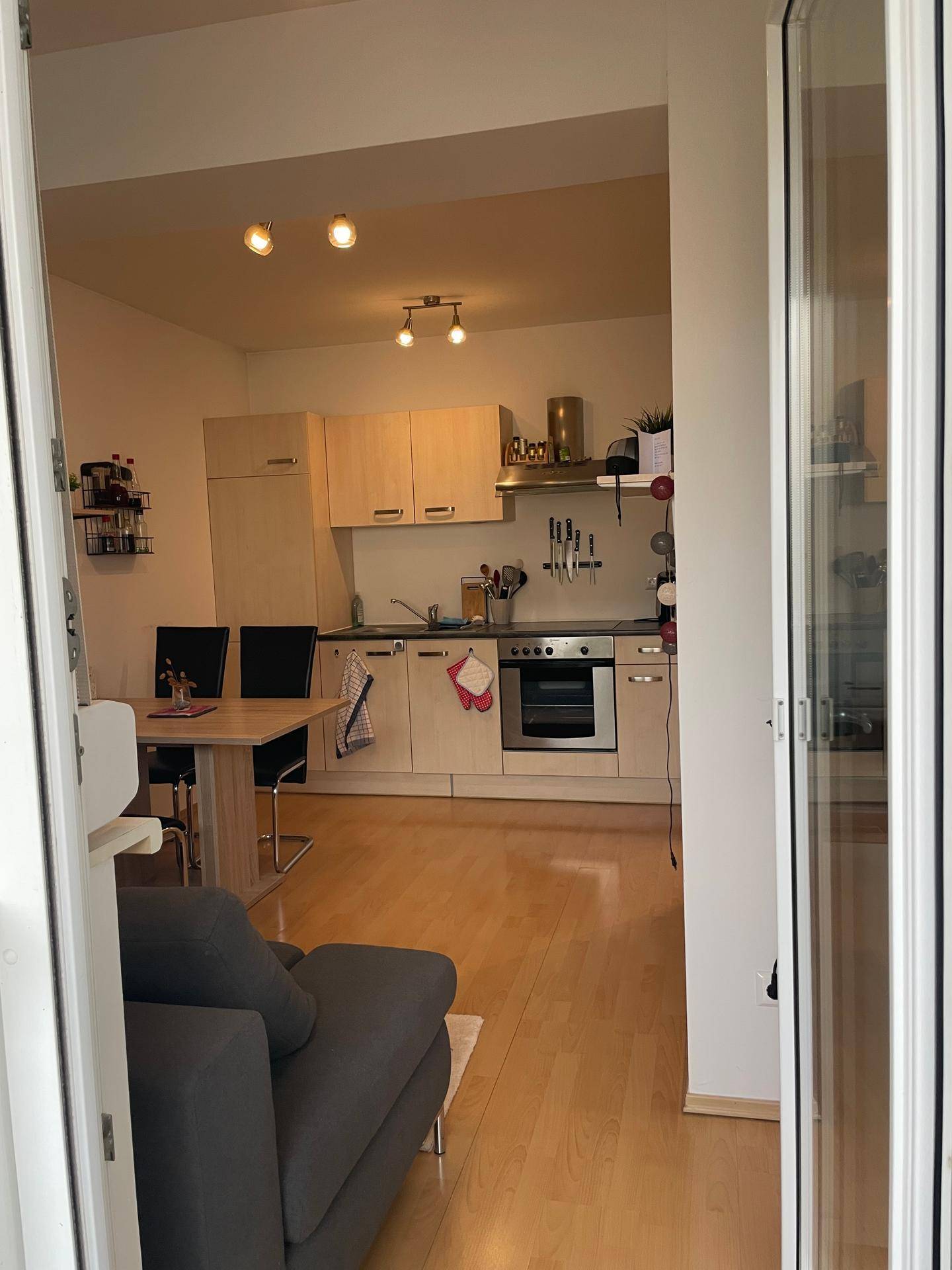 Blick vom Balkon in den offenen Wohn-, Ess- und Küchenbereich mit hellem Laminat.