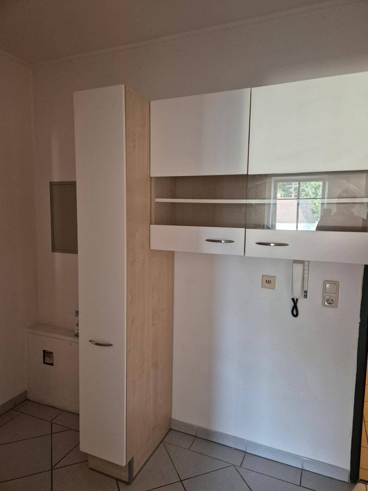 Küchenbereich mit weißen und hellen Holzschränken, gefliestem Boden und einem Fenster.