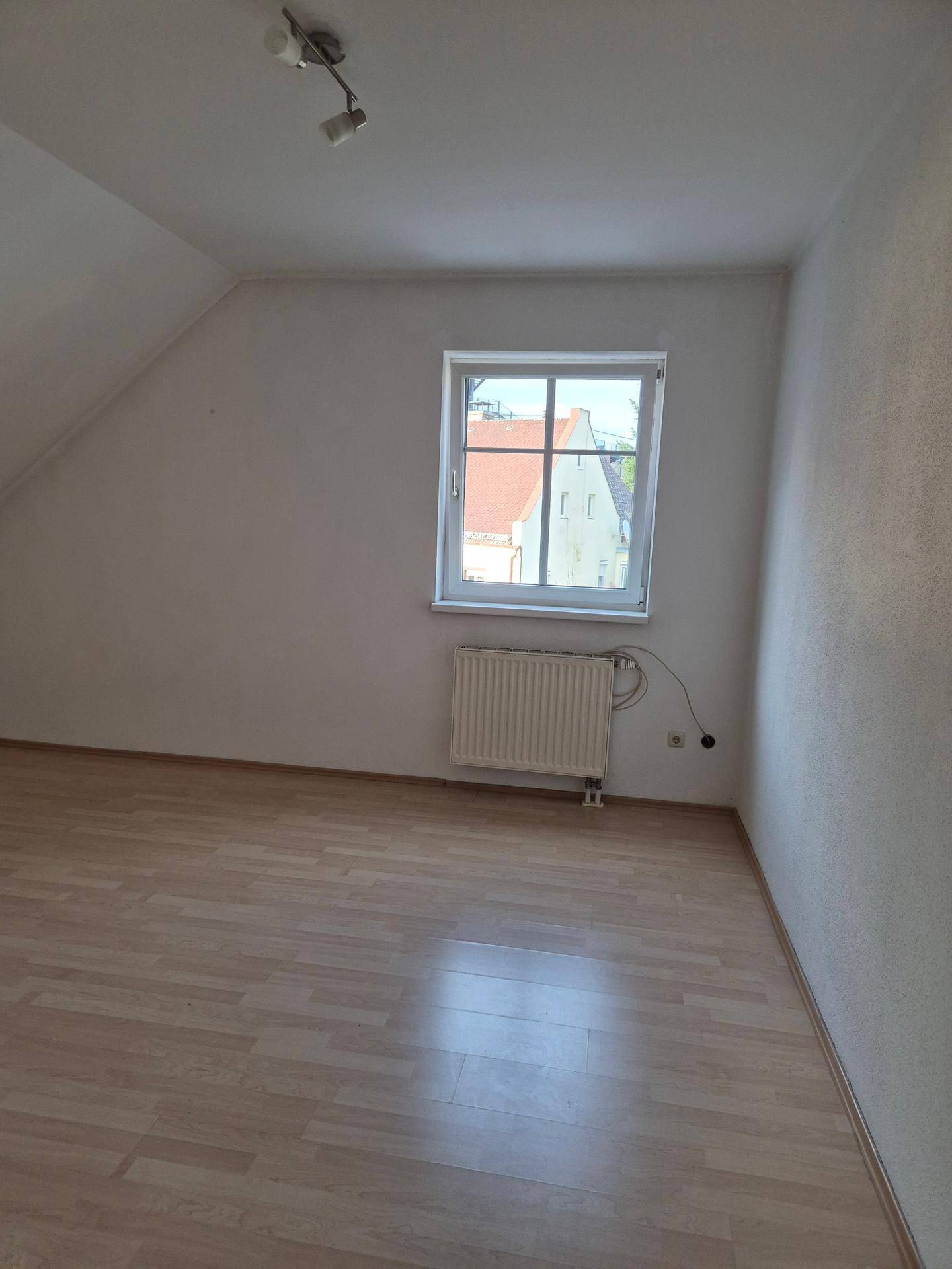 Heller Dachbodenraum mit Dachschräge, Laminatboden, Fenster und Heizkörper.