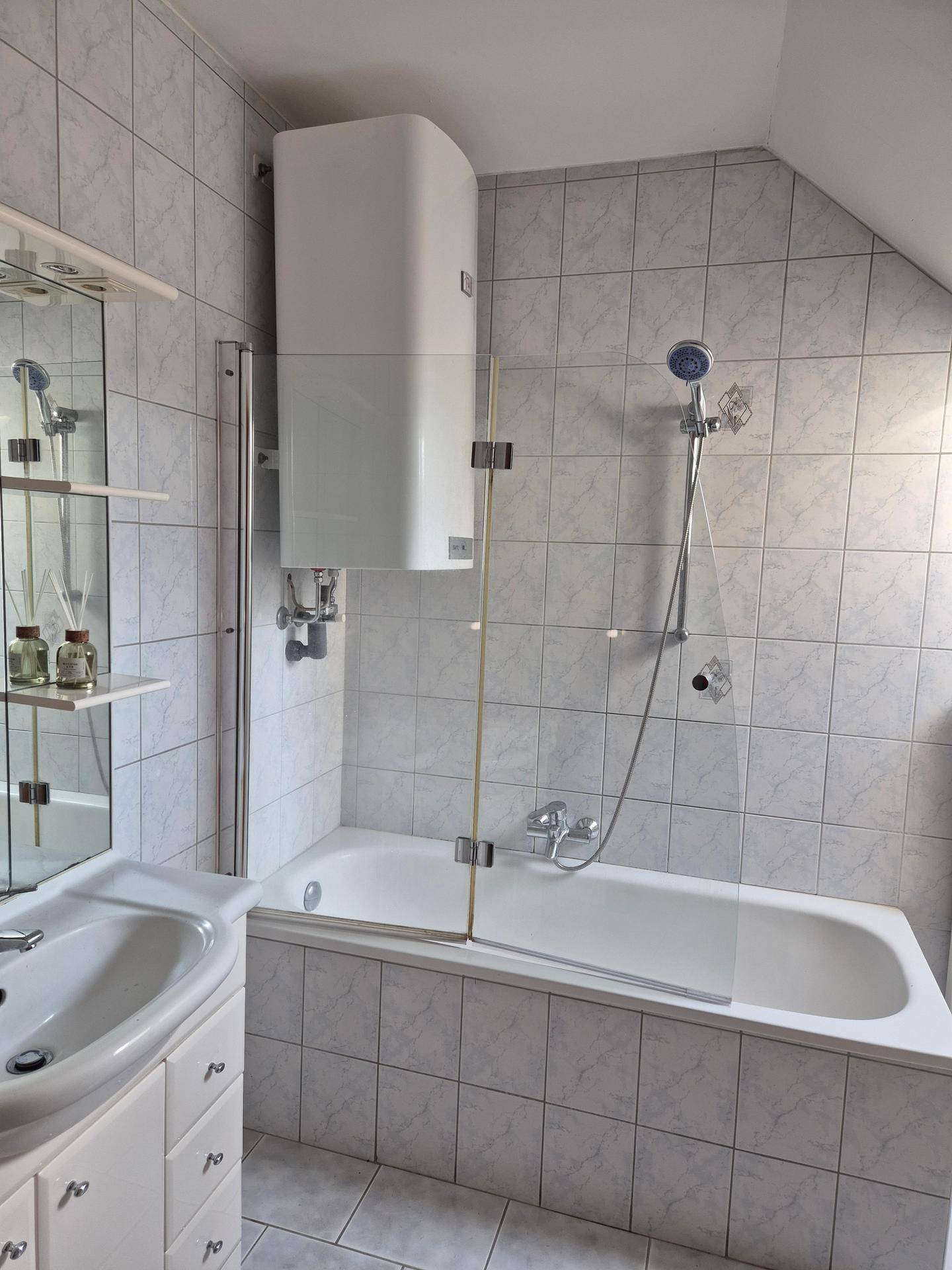 Badezimmer mit Waschbecken, Badewanne mit Duschwand, Wandheizkörper und gefliesten Oberflächen.