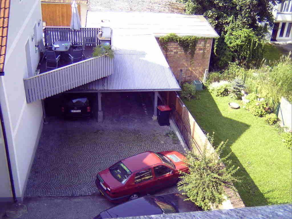 Blick von oben auf einen Hinterhof mit gepflastertem Parkplatz, Carport und einer möblierten Terrasse.