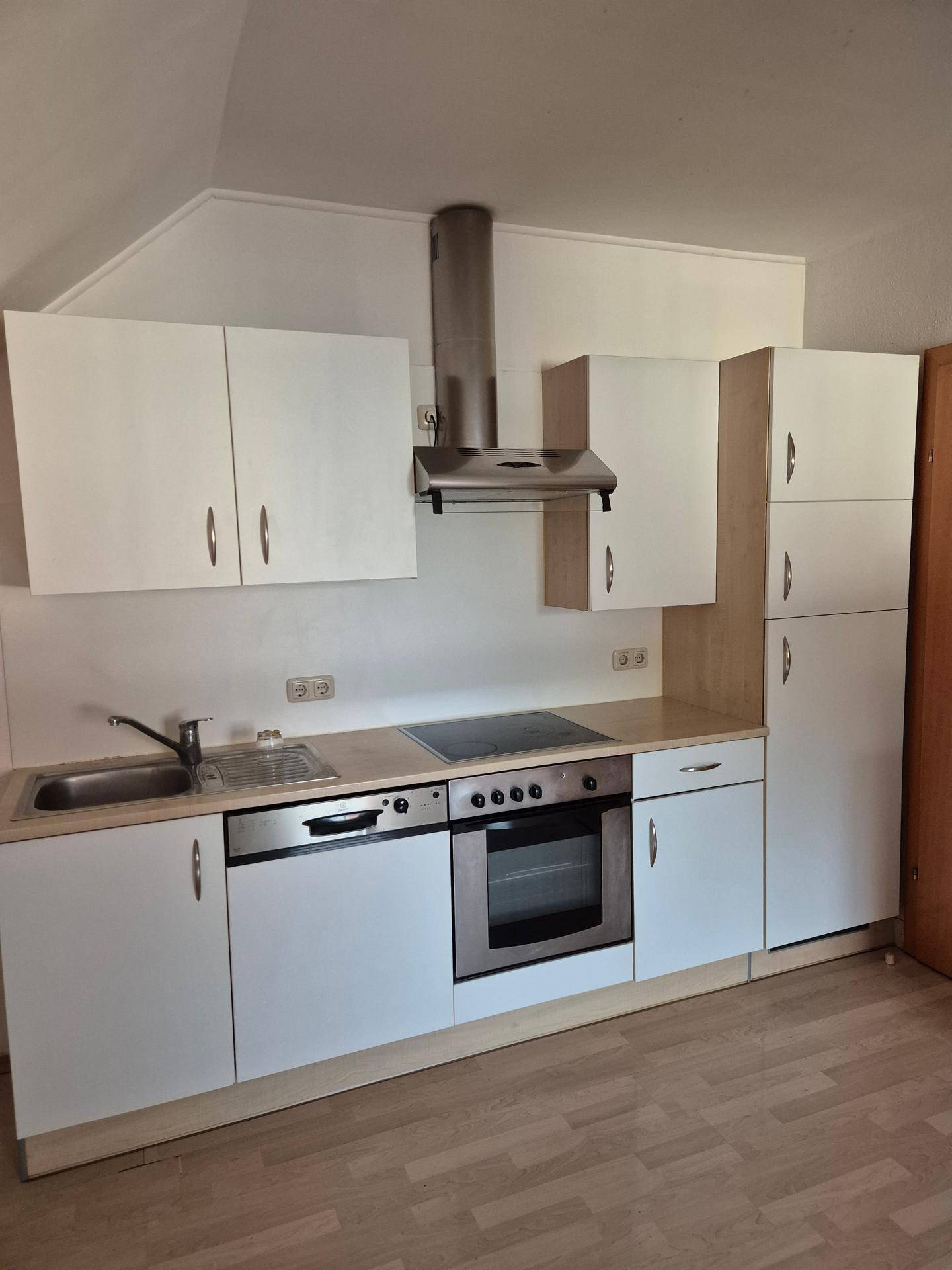 Küche mit weißen Schränken, Laminatarbeitsplatte und Einbaugeräten unter Dachschräge.