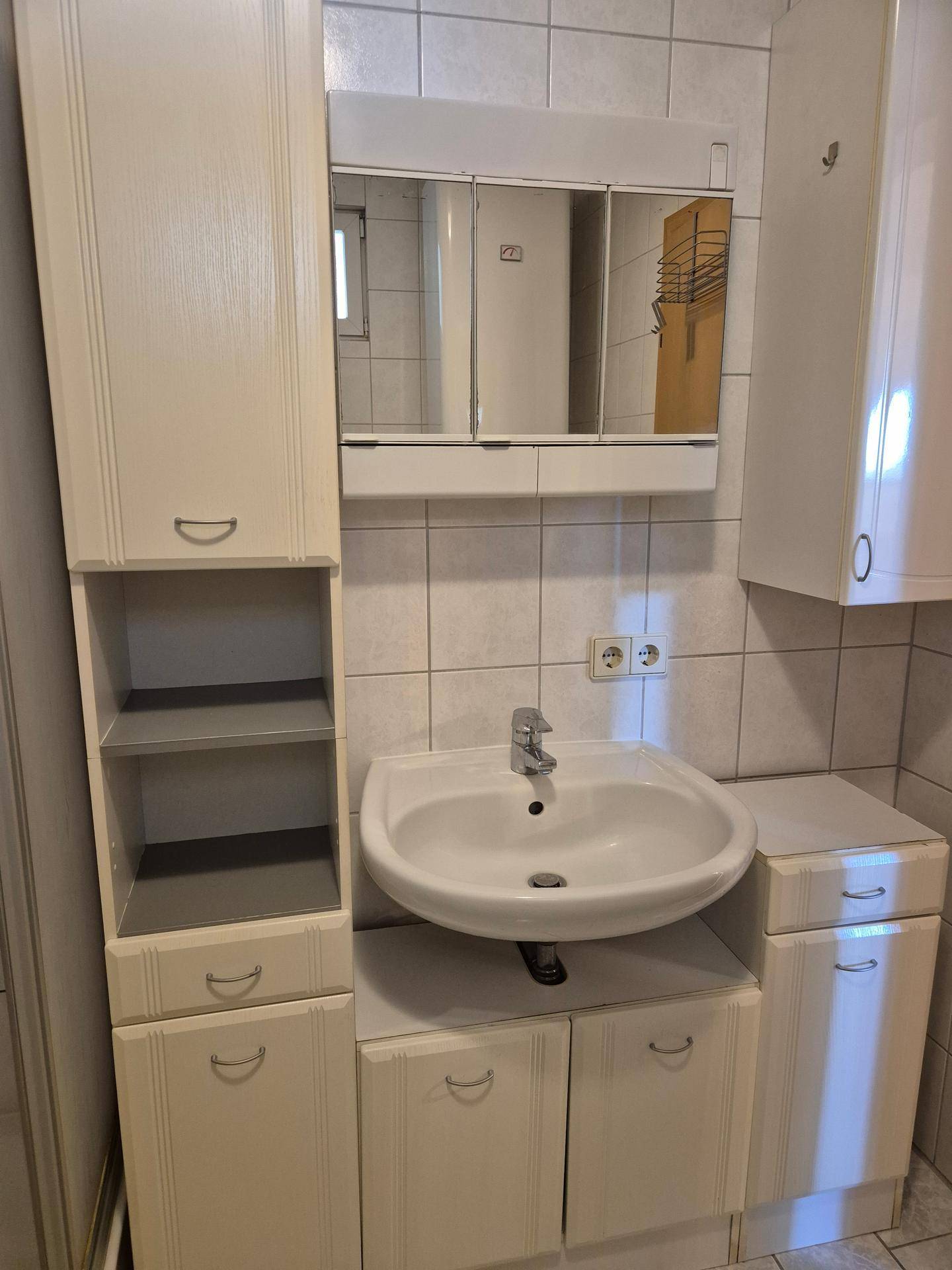 Badezimmer mit weißem Waschbecken, Spiegelschrank und hellen Fliesen an den Wänden.