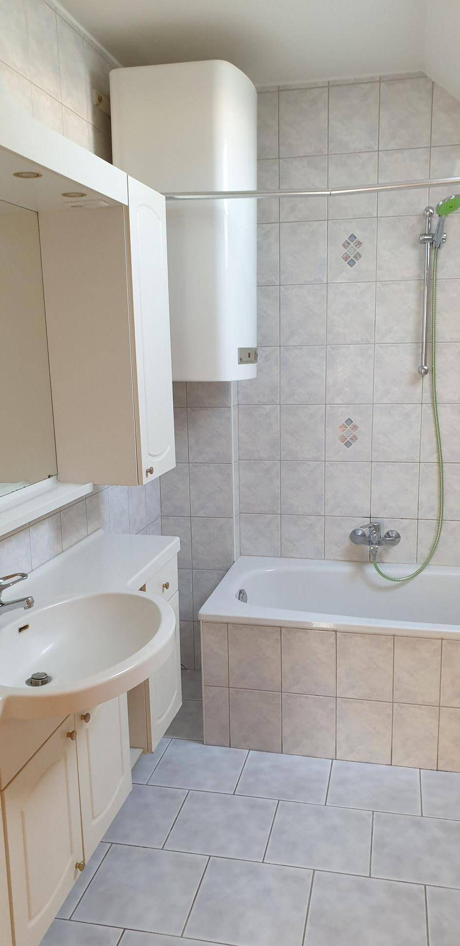Helles Badezimmer mit Badewanne, Waschbecken und Wandheizkörper, gefliesten Wänden und Boden.