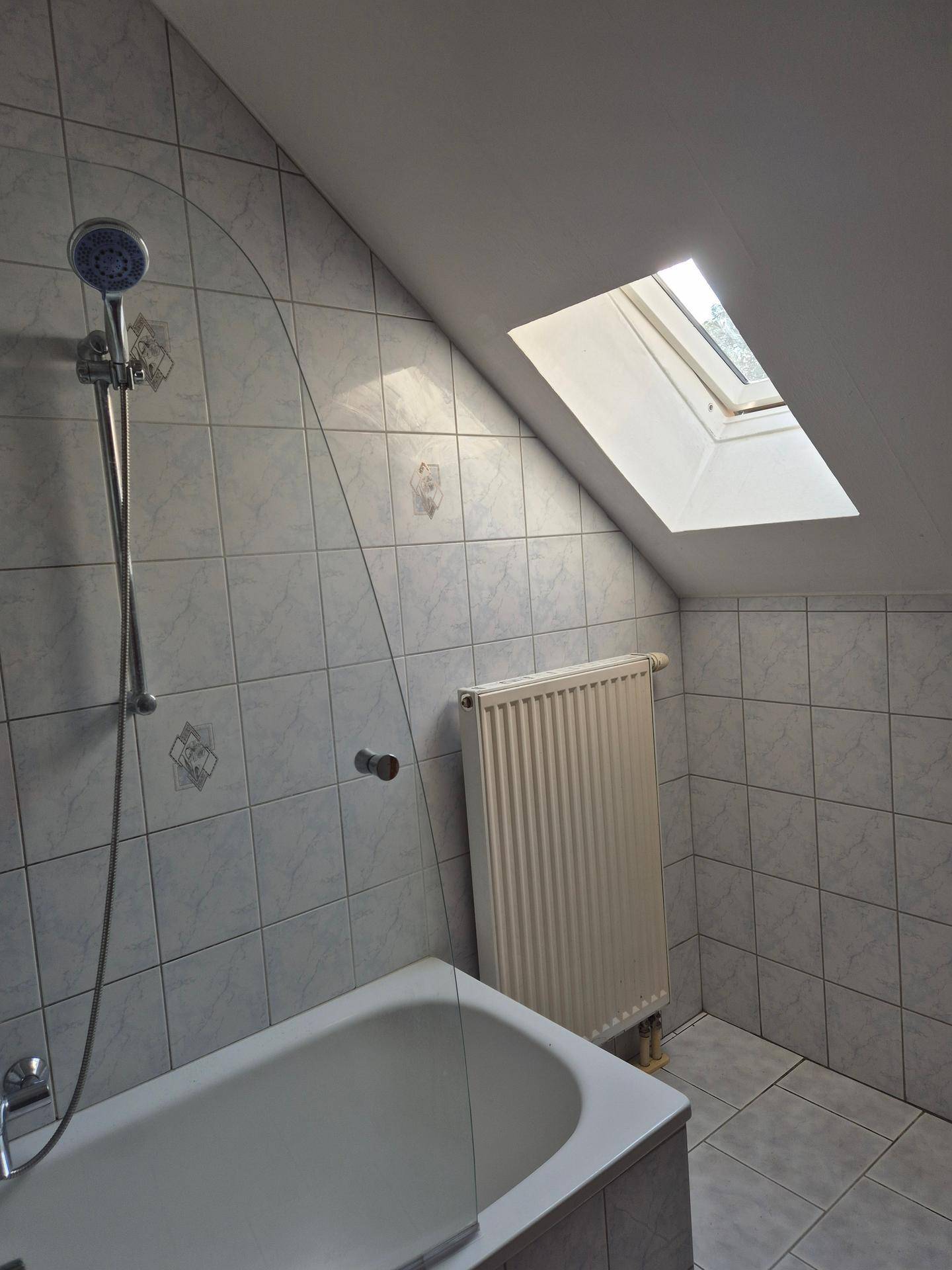 Badezimmer mit Badewanne, Duschkopf, gefliesten Wänden und Dachfenster in der Schräge.