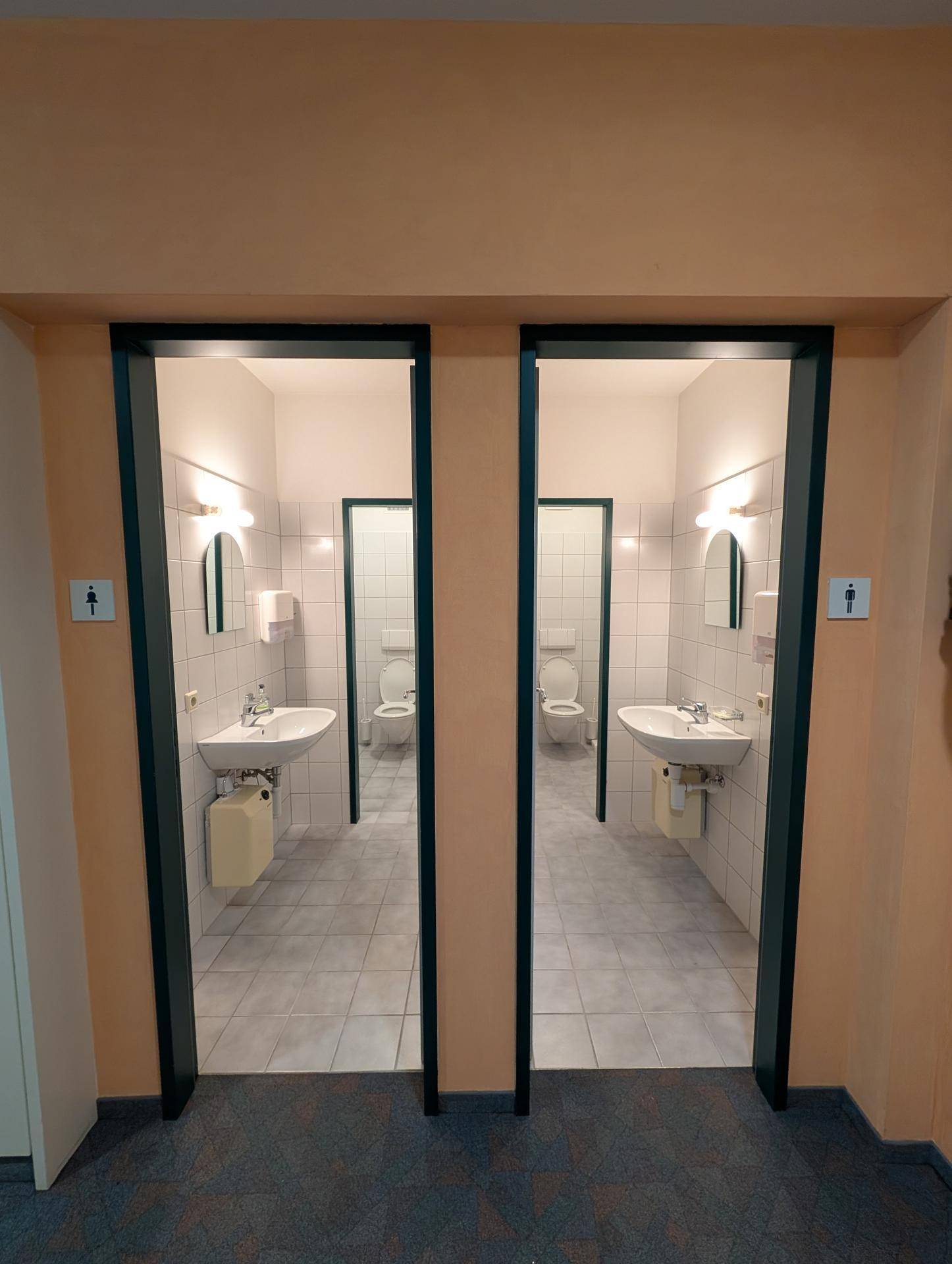 Zwei separate Toilettenräume mit Waschbecken und Spiegeln, hell gefliest und gut beleuchtet.