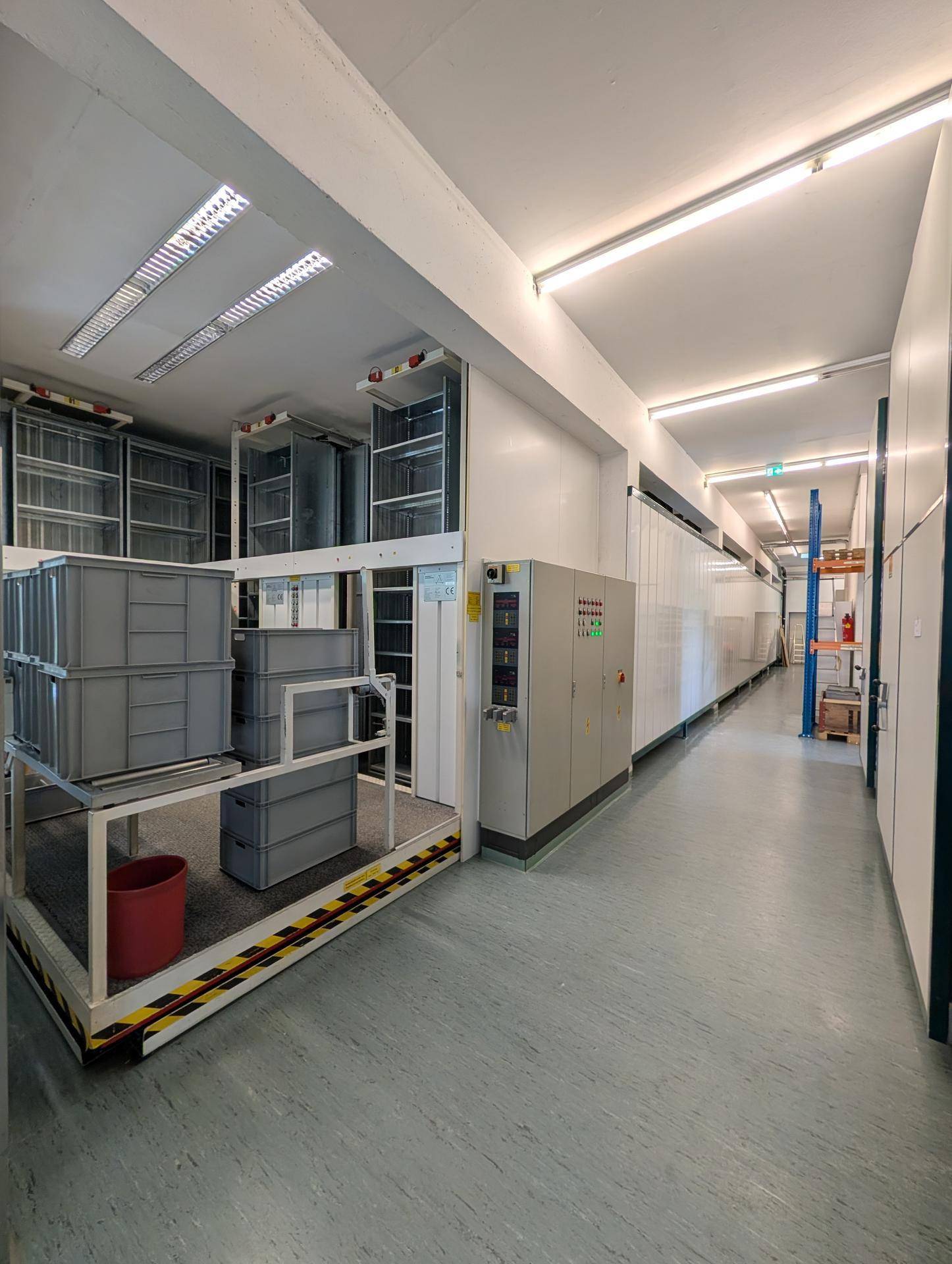 Langer Lagerflur mit Fördertechnik und Regalen, gut beleuchtet und funktional für Logistik eingerichtet.