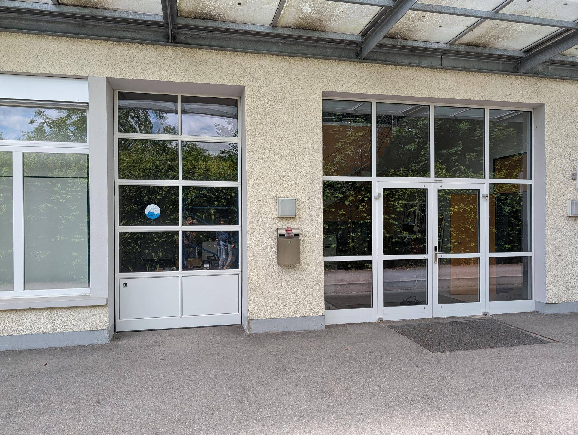 Gebäudefassade mit großen Fenstern und einer breiten Tür, die viel Tageslicht hereinlässt und modern wirkt.