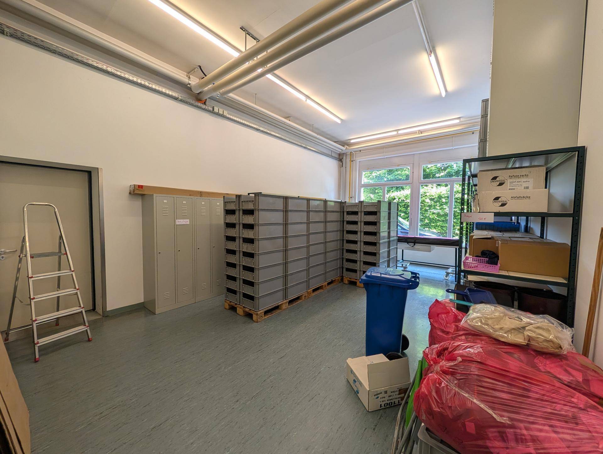 Lagerraum mit Spinden, Transportboxen und einem Fenster, das Tageslicht hereinlässt und den Raum erhellt.