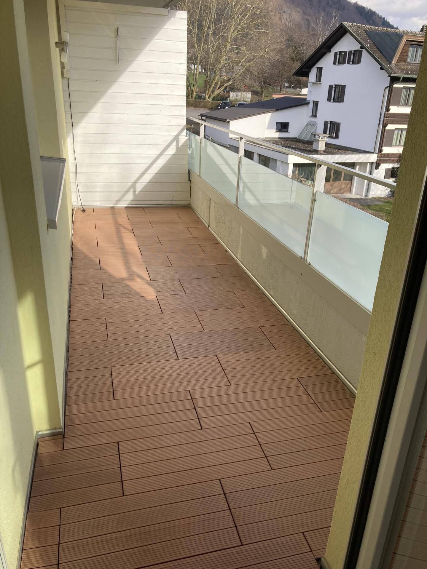 Geräumiger Balkon mit Holzdielenboden und Glasgeländer, ideal für entspannte Stunden im Freien.