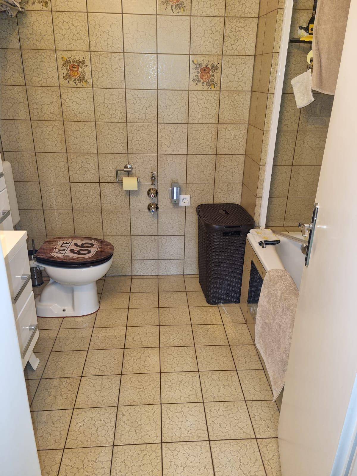 Badezimmer mit Badewanne, WC und gefliesten Wänden in hellem Farbton.