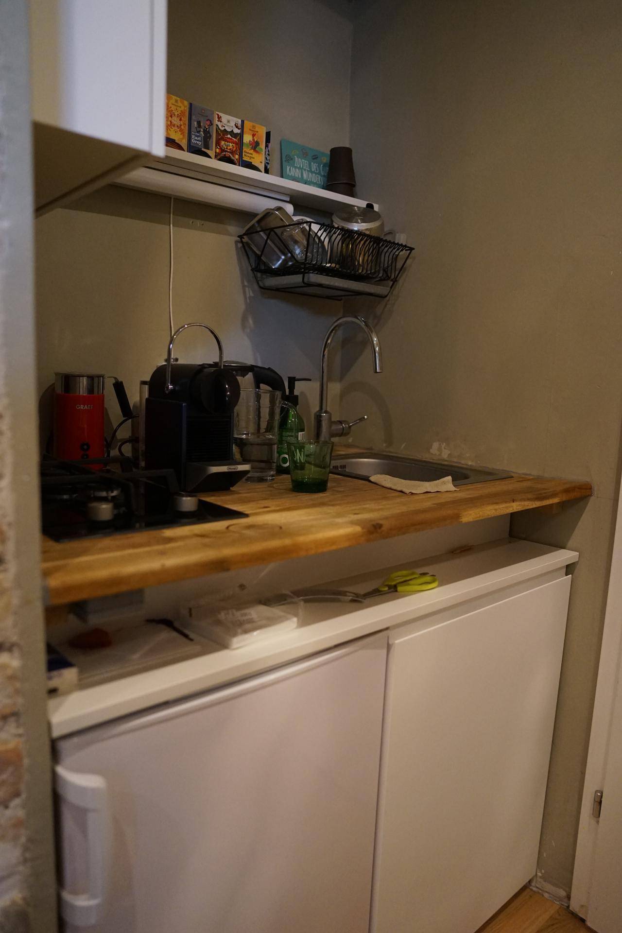 Kleine Küchenzeile mit Holzarbeitsplatte, Spüle, Kaffeemaschine und Unterbaukühlschrank.