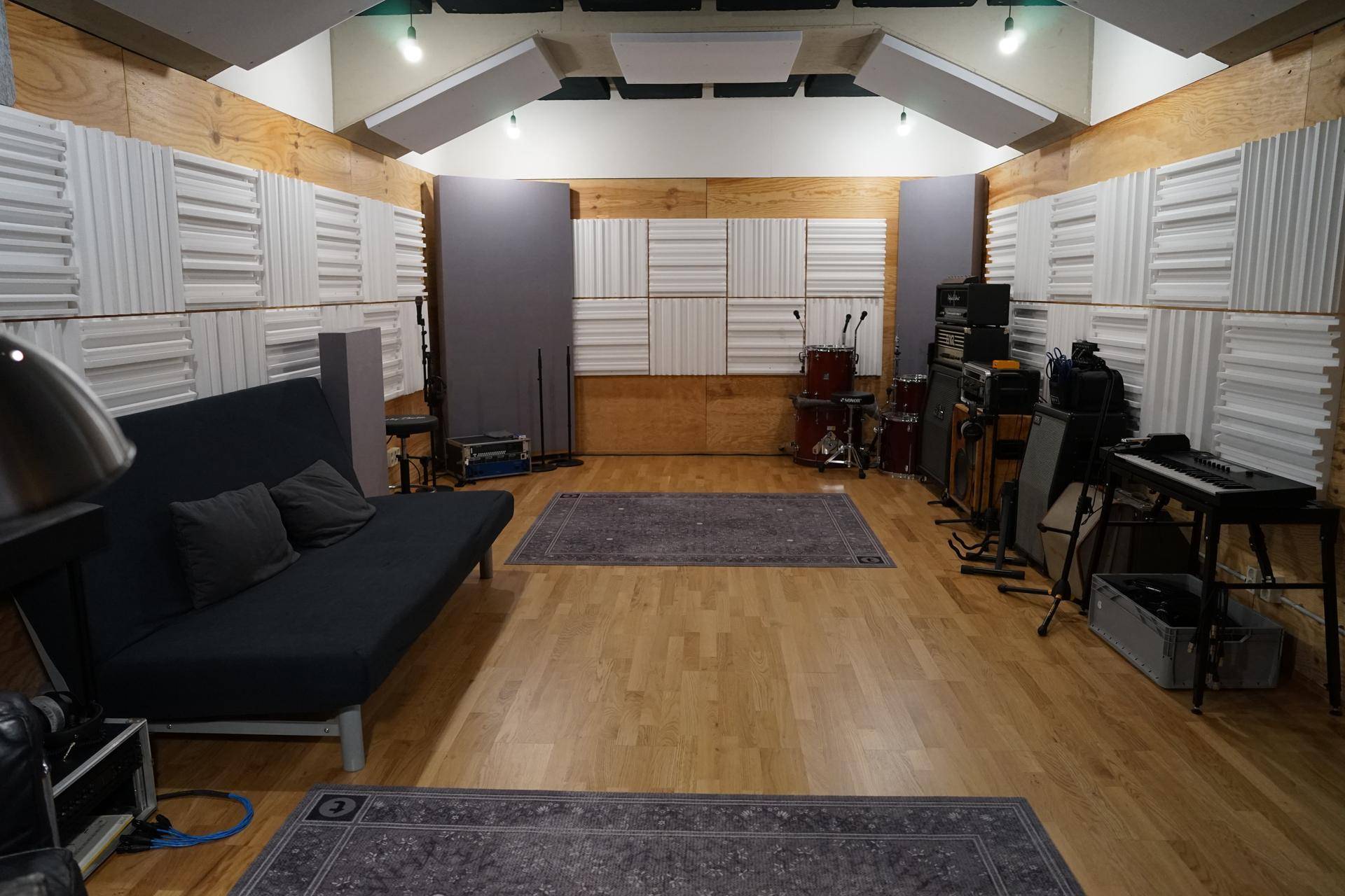 Breiter Blick auf den Aufnahmeraum mit schallabsorbierenden Paneelen, Sofa und Holzboden für optimale Akustik.