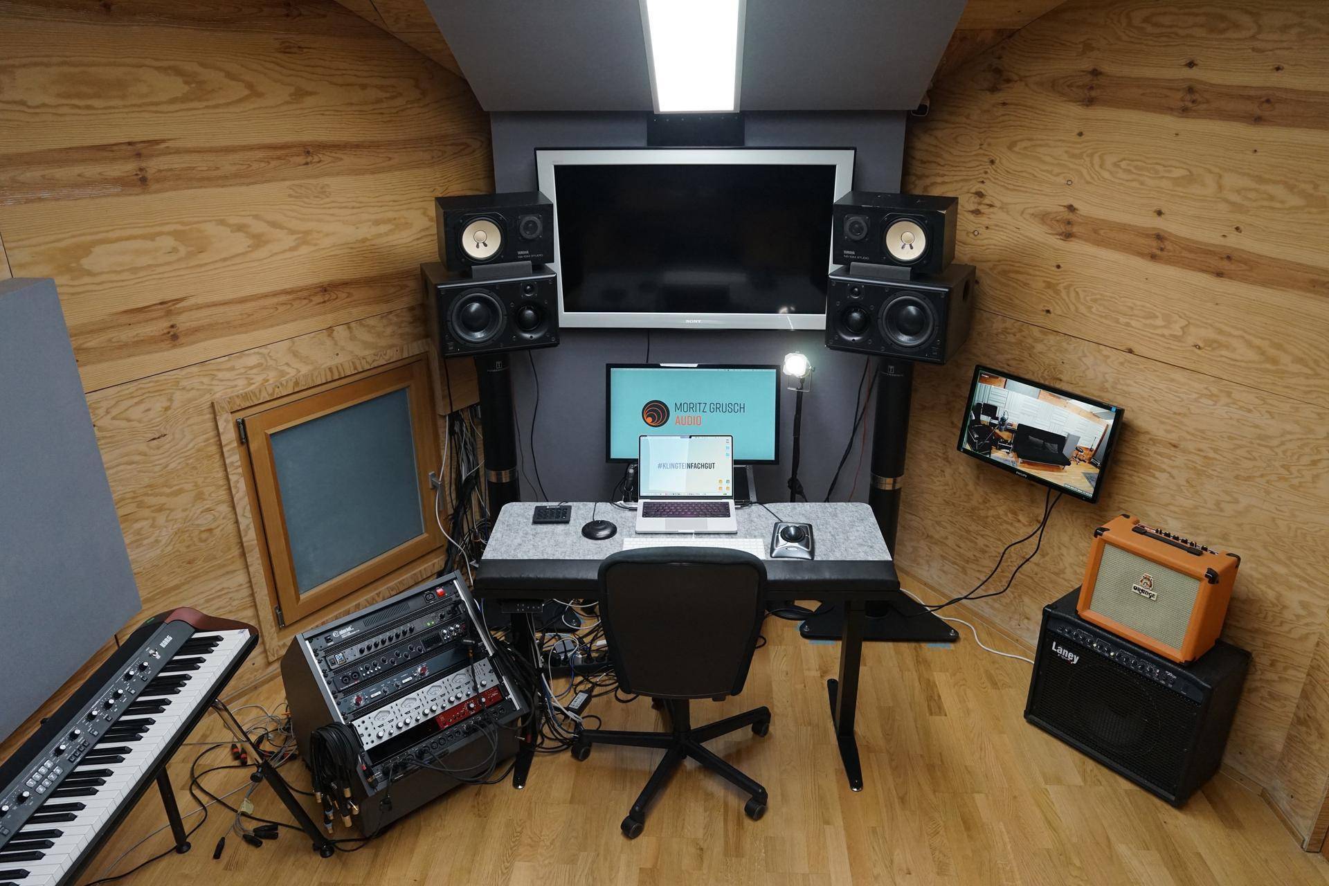 Kontrollraum eines Musikstudios mit Holzwänden, Schreibtisch, Monitoren und professioneller Audioausrüstung.