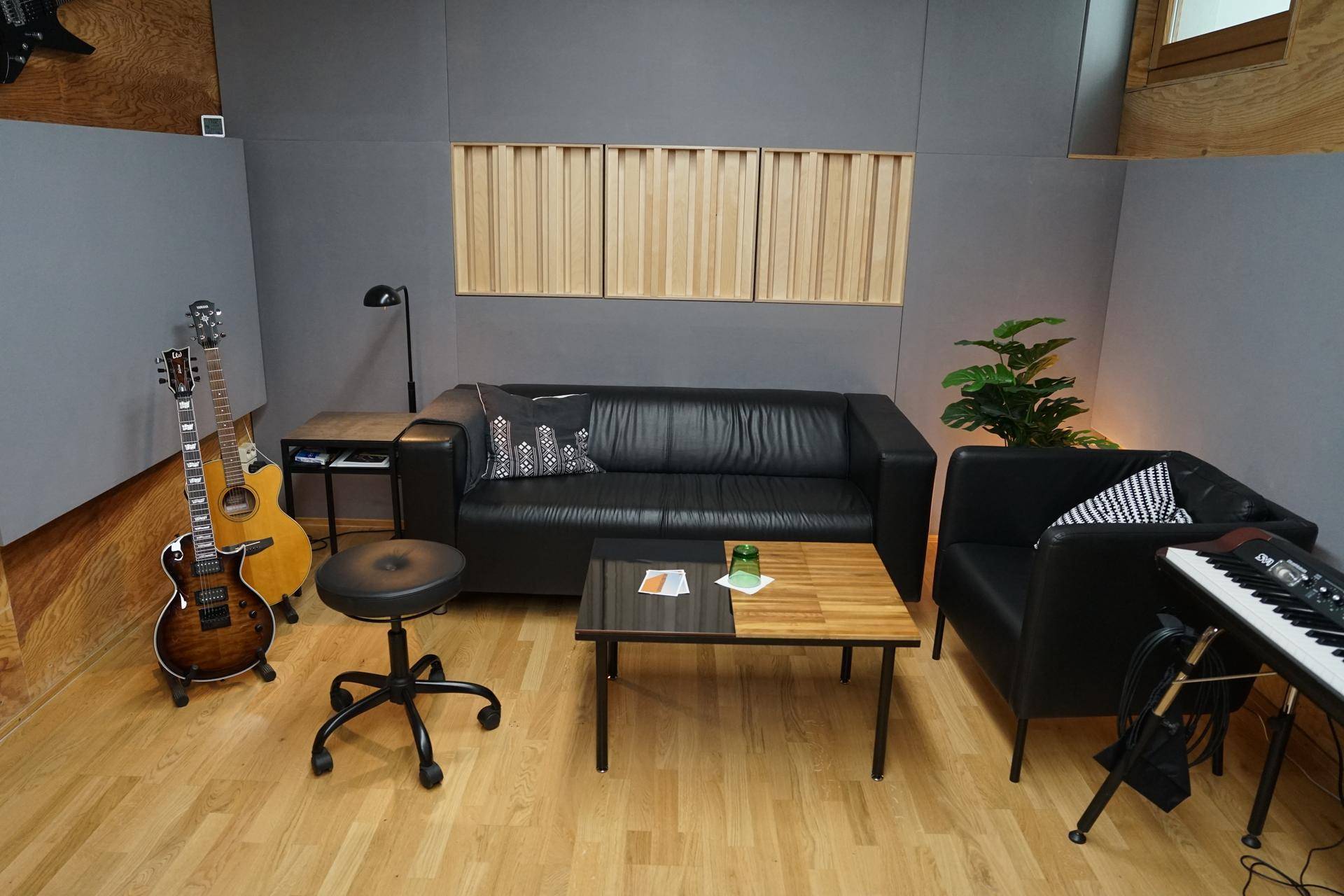 Gemütlicher Lounge-Bereich im Studio mit schwarzem Ledersofa, Gitarren und Holzboden für entspannte Pausen.