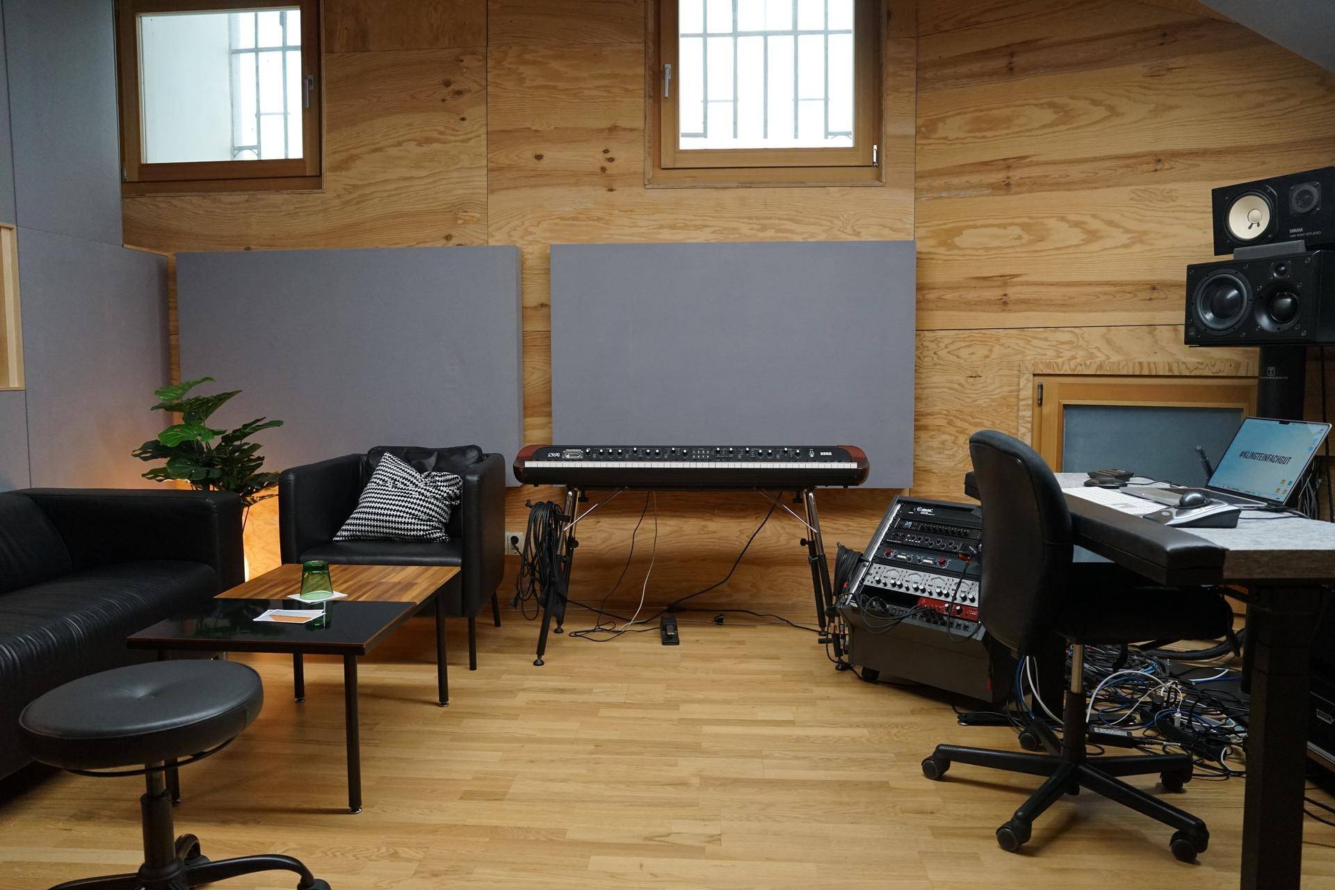 Kombinierter Lounge- und Arbeitsbereich im Studio mit Ledersofa, Keyboard und Audio-Rack.
