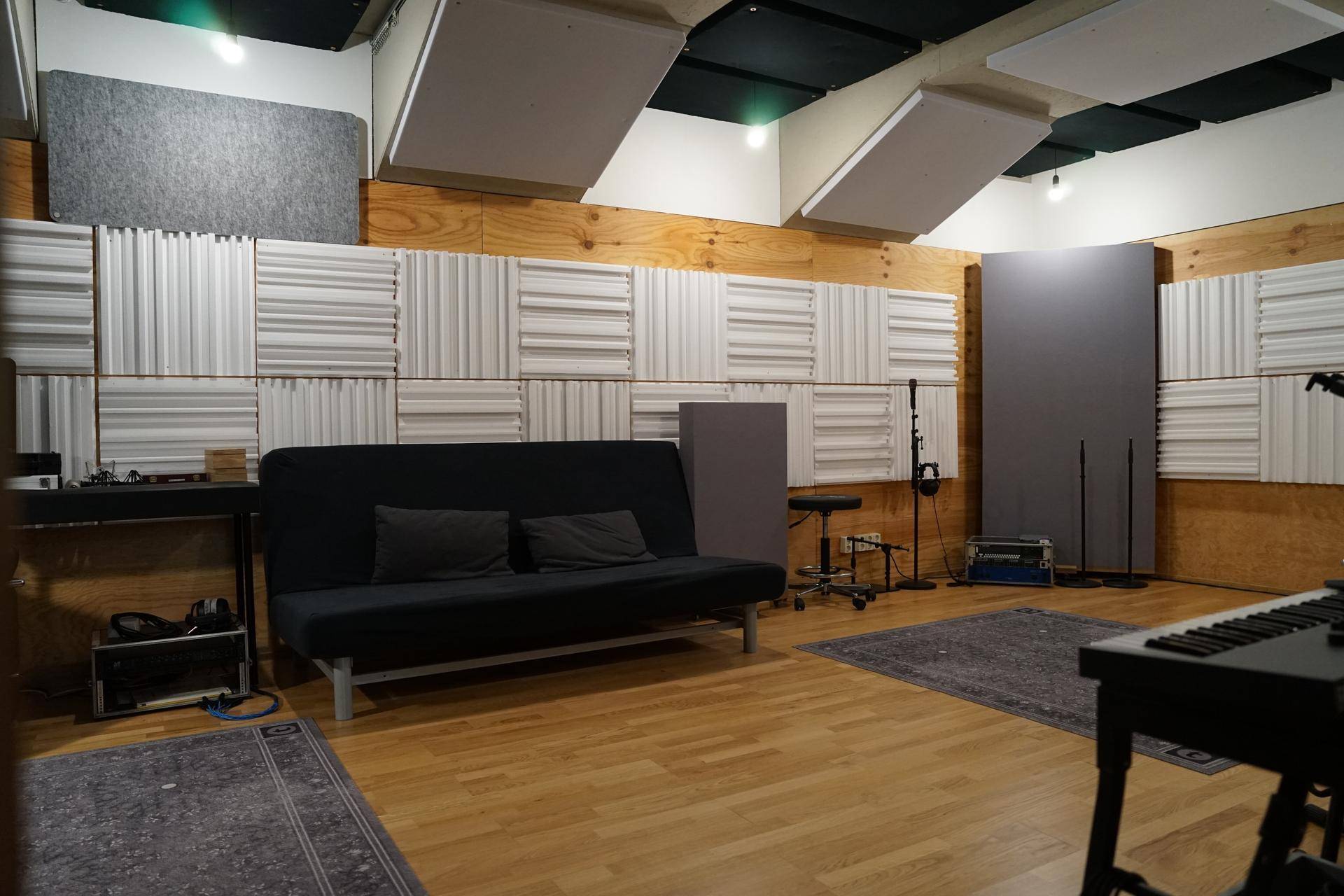 Geräumiger Aufnahmeraum mit akustischen Paneelen, bequemer Couch und Holzboden für Musikproduktionen.