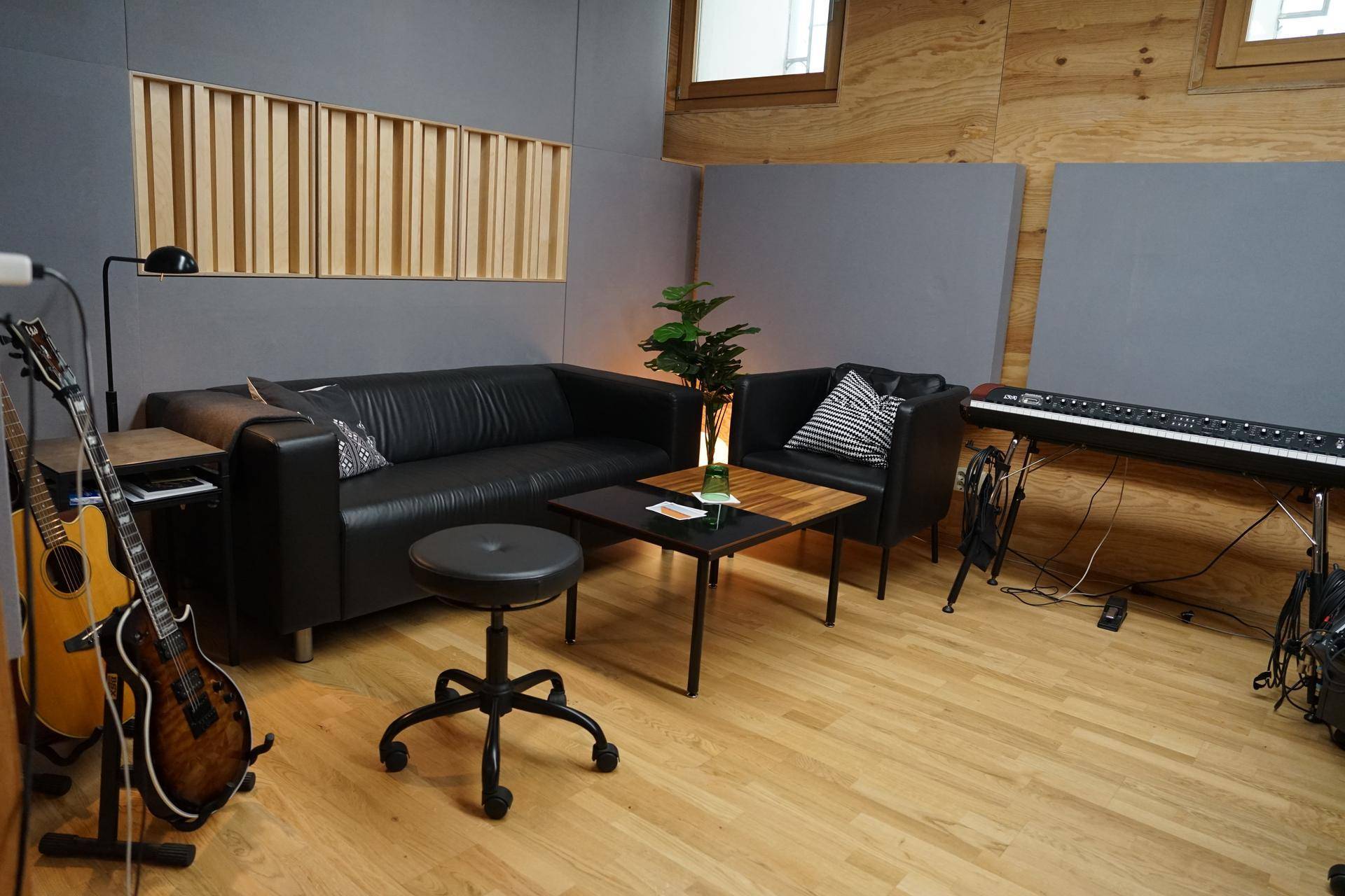 Studio-Lounge mit schwarzem Ledersofa, Gitarren und Holzboden, ideal für kreative Pausen und Entspannung.