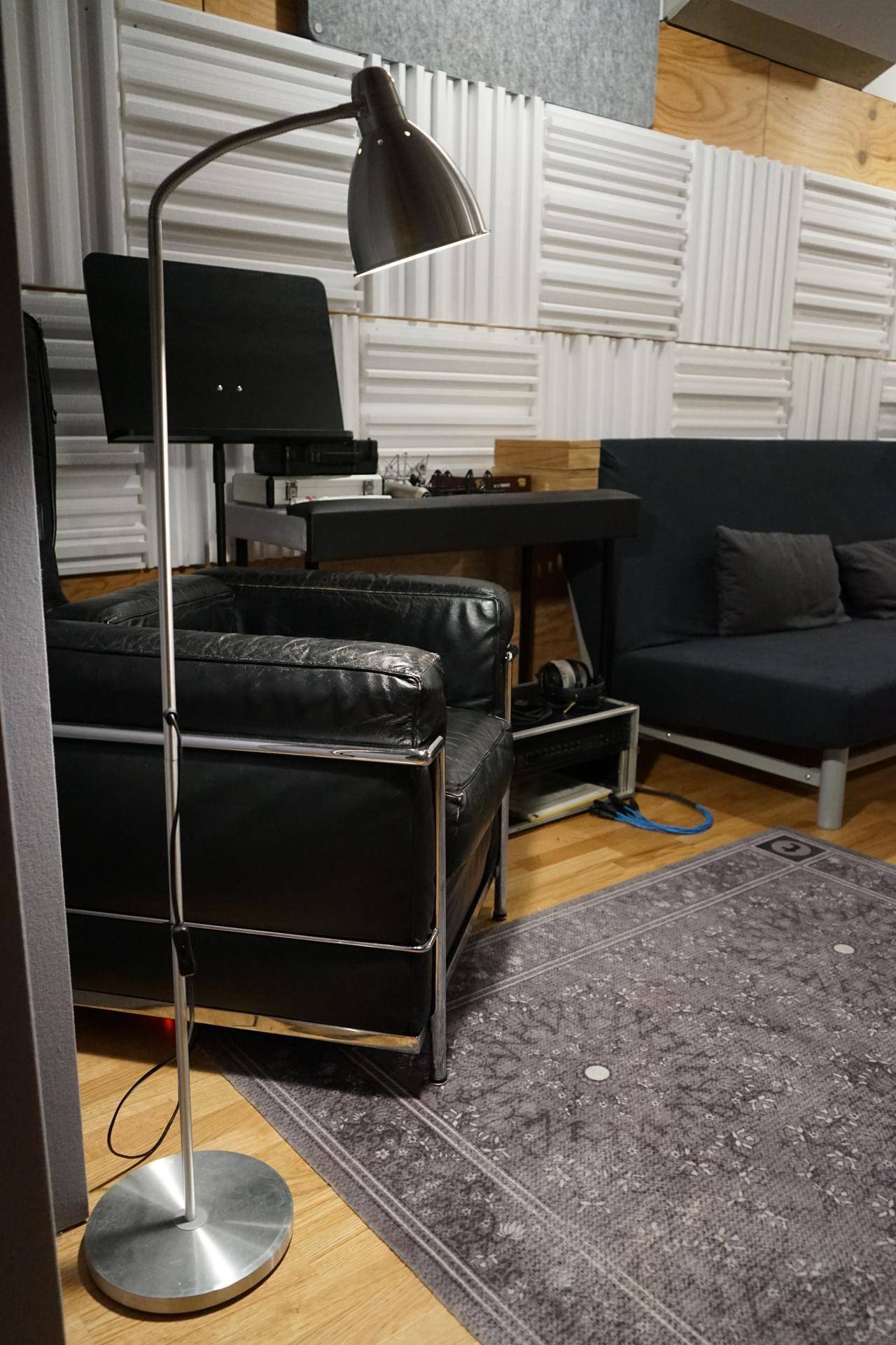 Stehlampe neben einem schwarzen Ledersessel und einem gemusterten Teppich im Studiobereich.