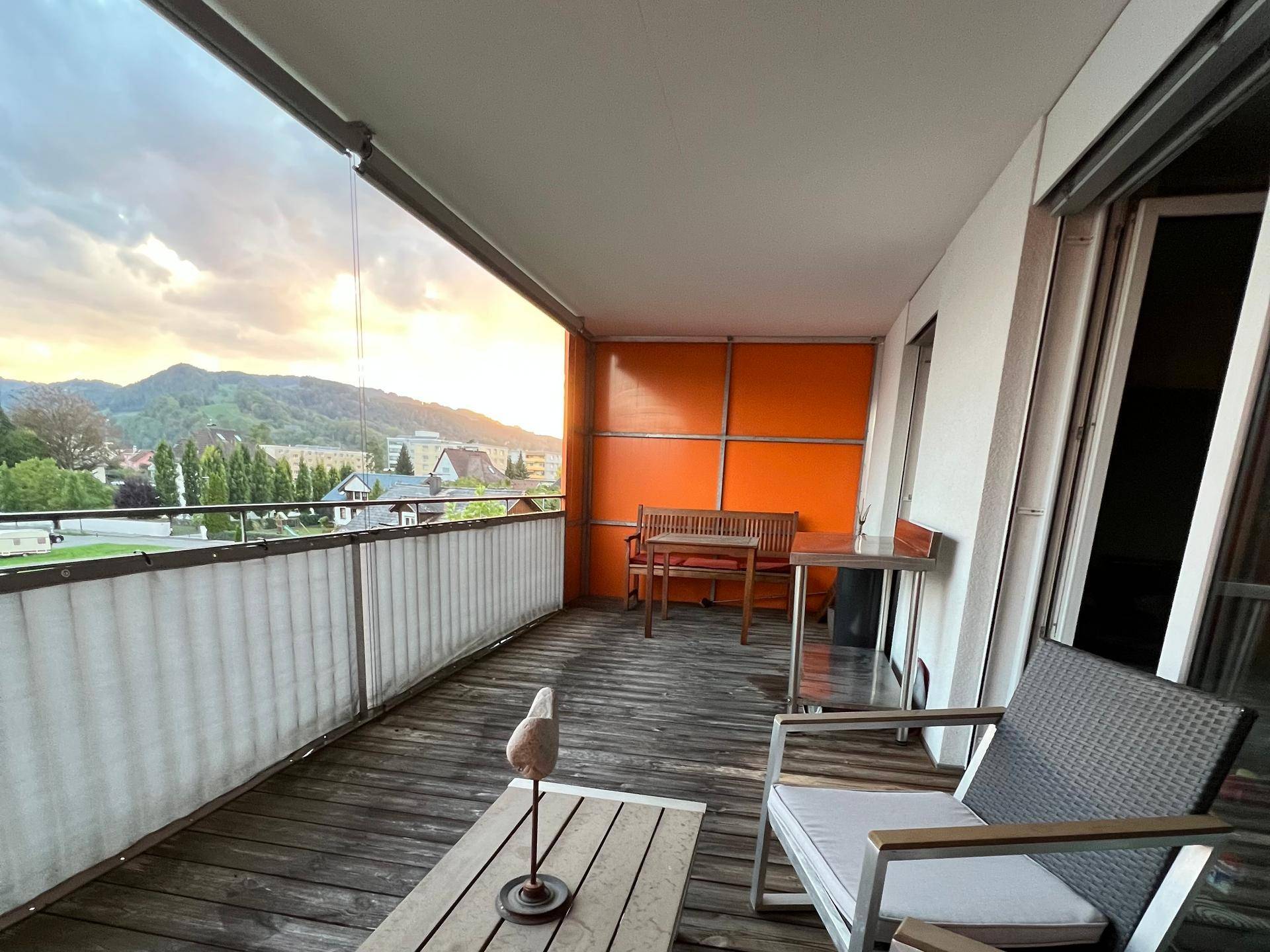 Geräumiger Balkon mit Holzboden, Sitzgelegenheiten und weitem Blick auf die Berge.