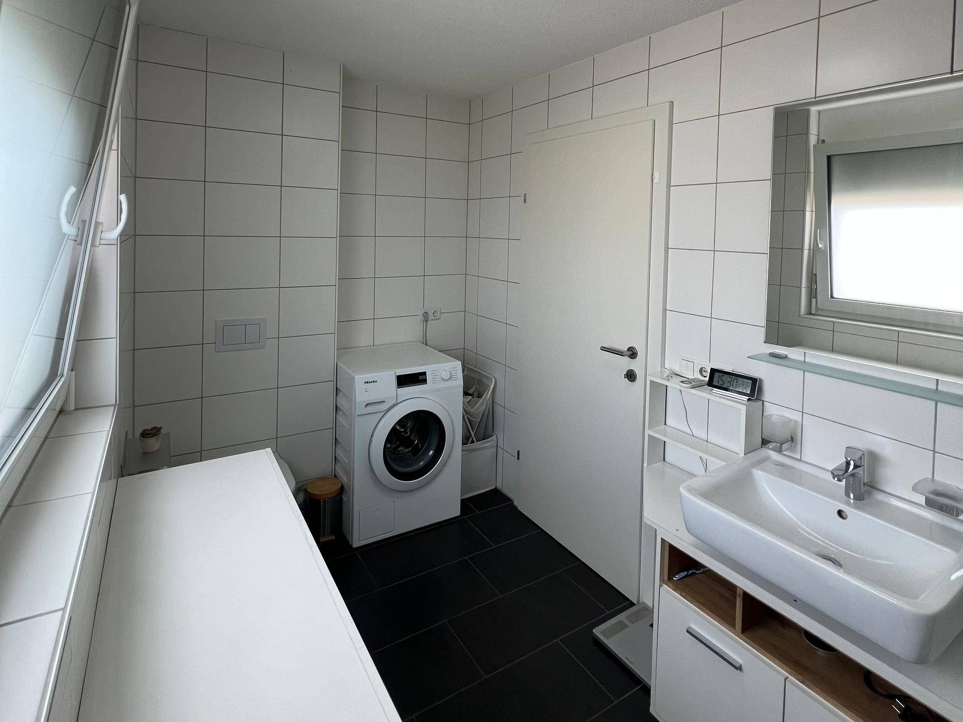 Helles Badezimmer mit Waschmaschine, Waschbecken und großem Fenster.