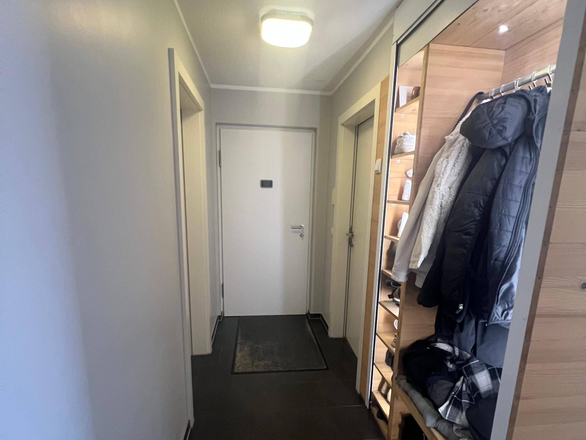 Heller Flur mit Garderobe, Holzelementen und dunklem Fliesenboden.