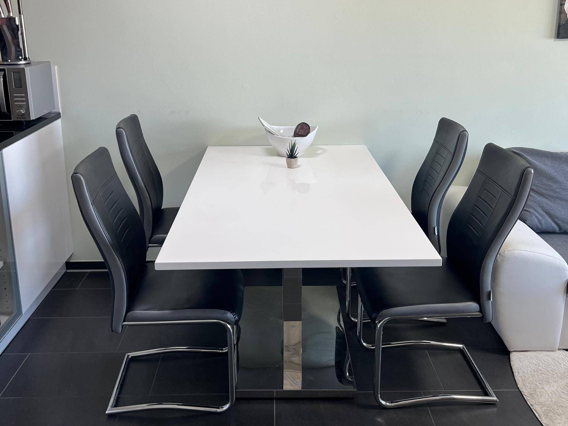 Moderner Essbereich mit weißem Tisch und schwarzen Stühlen, integriert in den Wohnraum.