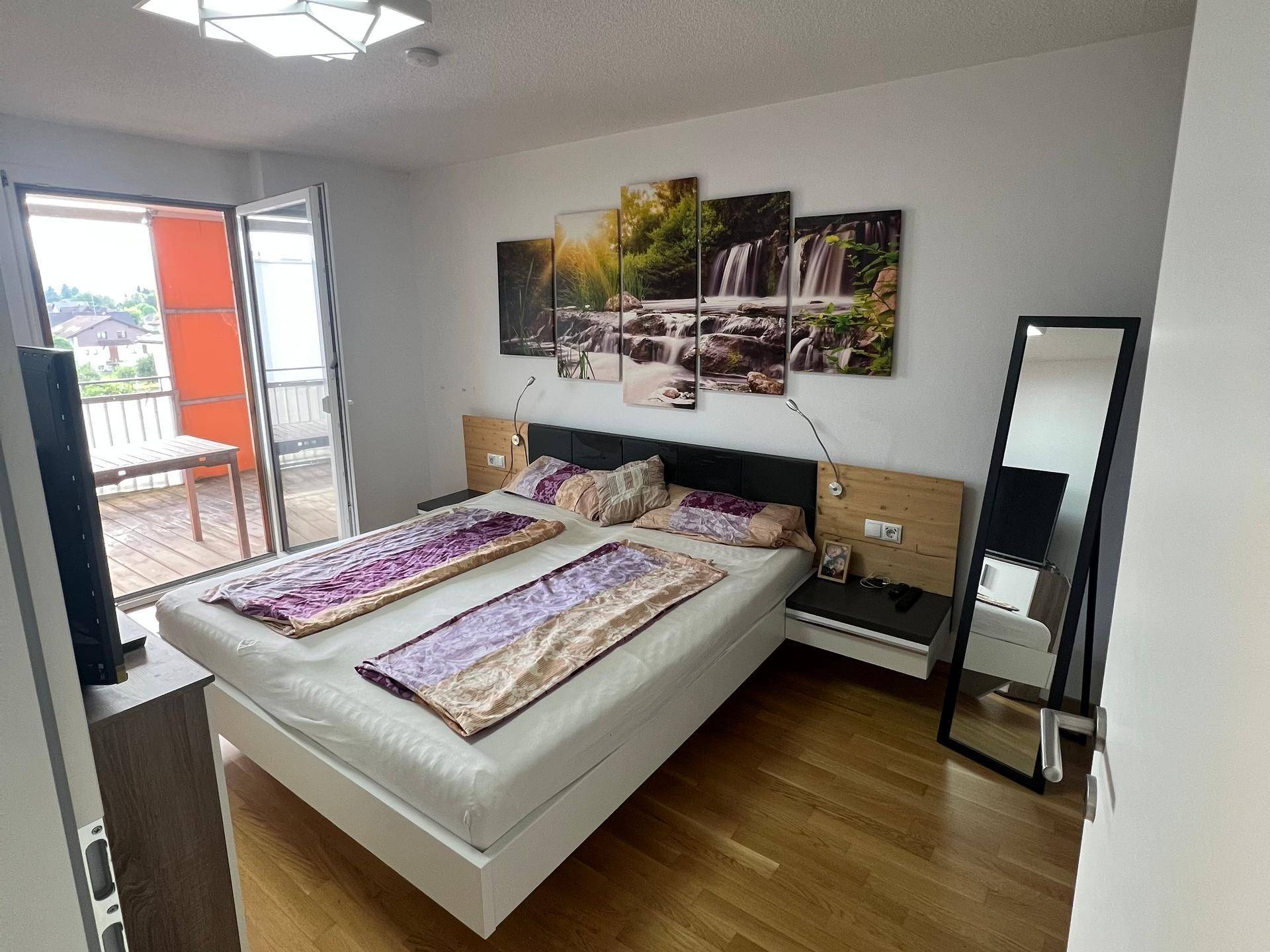 Schlafzimmer mit Doppelbett, Holzboden und Zugang zu einem möblierten Balkon.
