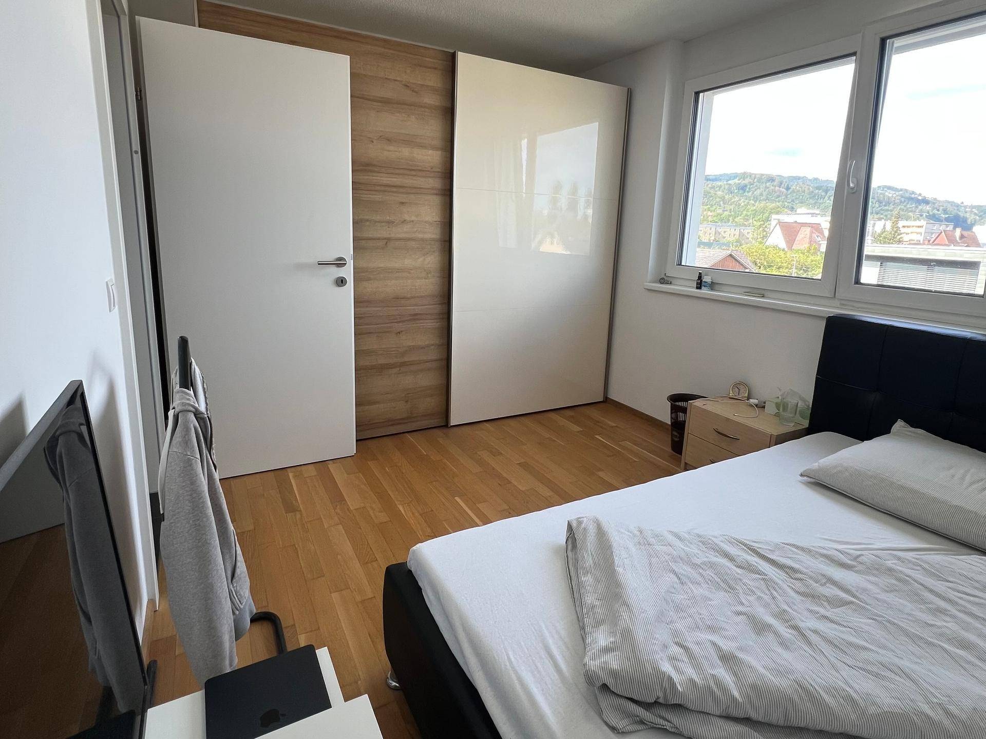 Schlafzimmer mit Holzboden, Schiebetürenschrank und Fenster mit Ausblick.