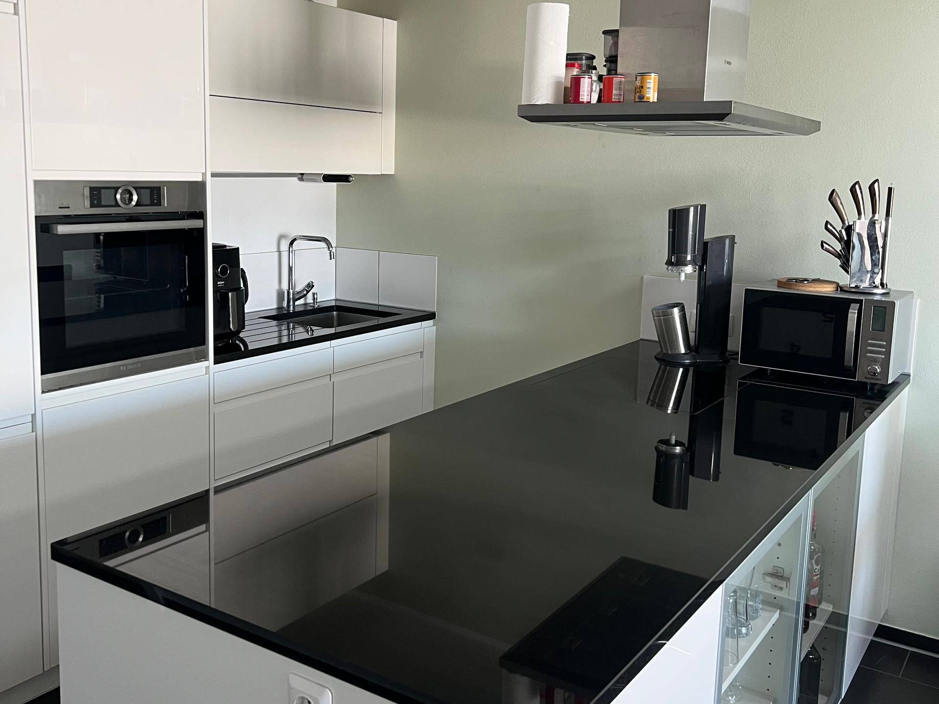 Moderne Küche mit schwarzen Arbeitsplatten, weißen Hochglanzfronten und integrierten Geräten.