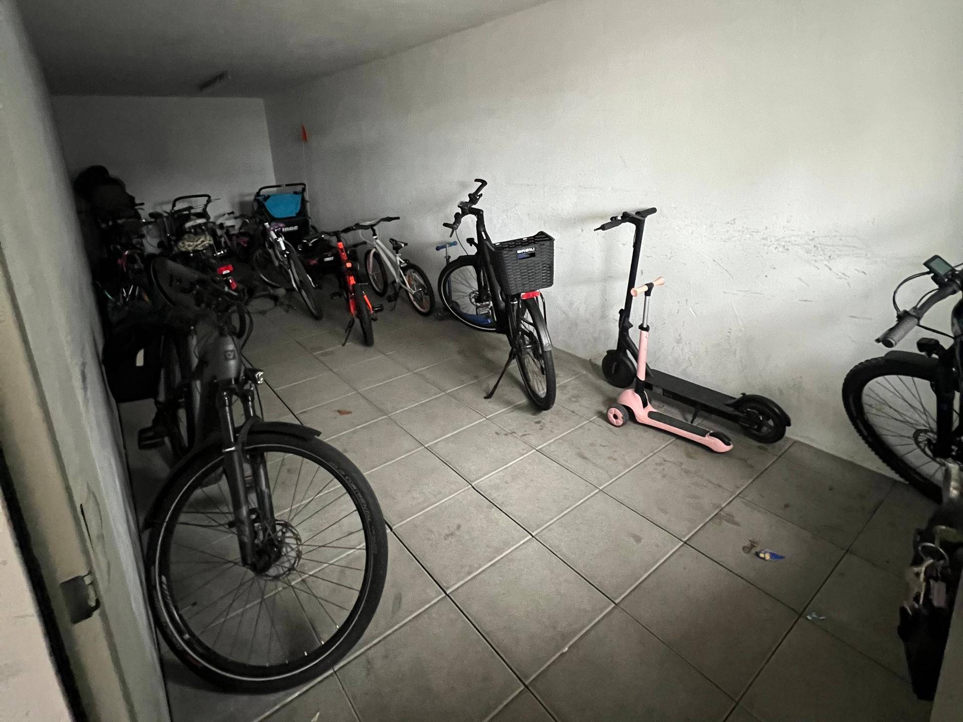 Fahrradraum mit Fliesenboden und verschiedenen Fahrrädern und Rollern.