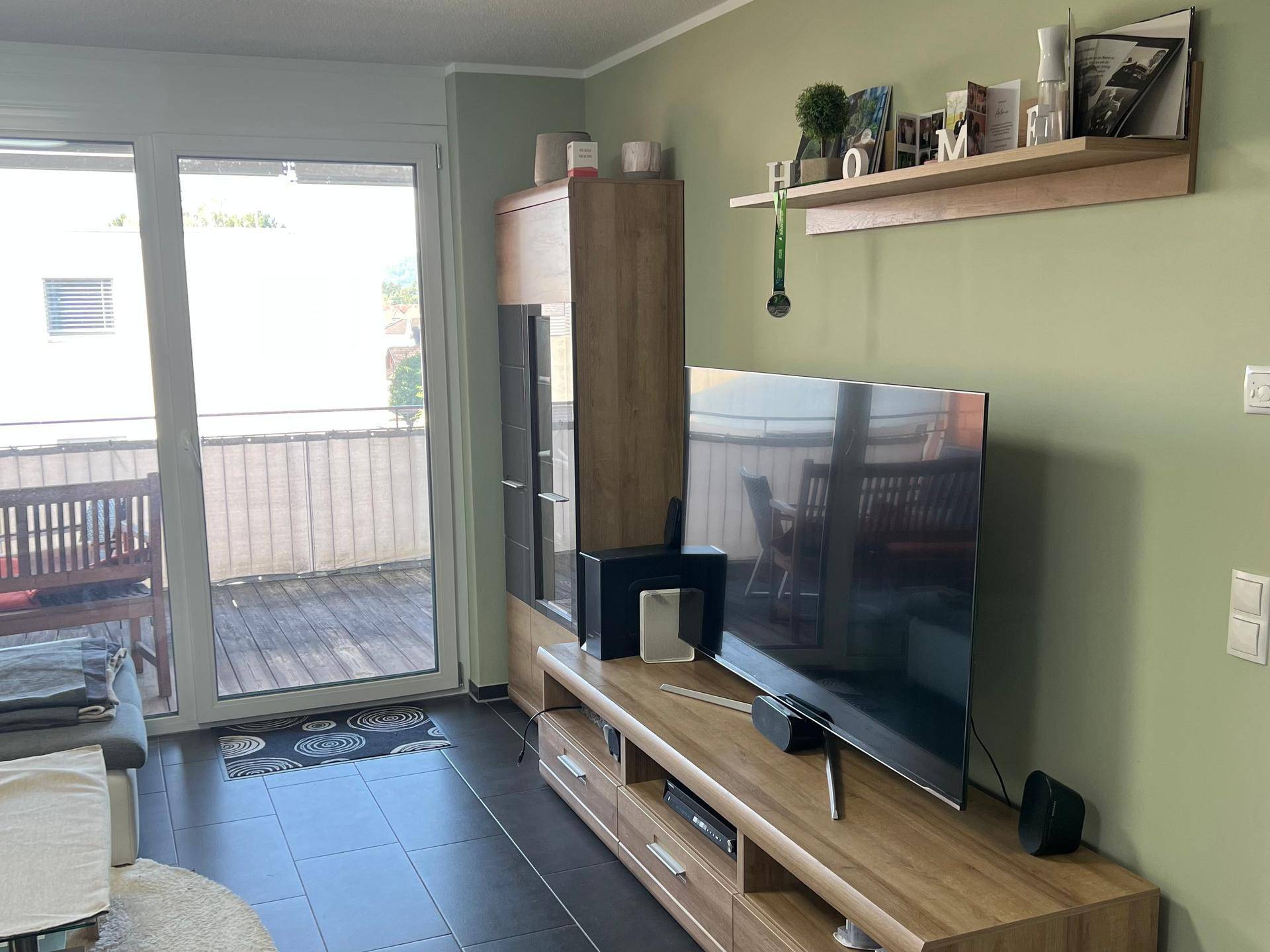 Wohnzimmer mit großem Fernseher, Holzmöbeln und Zugang zu einem Außenbereich.