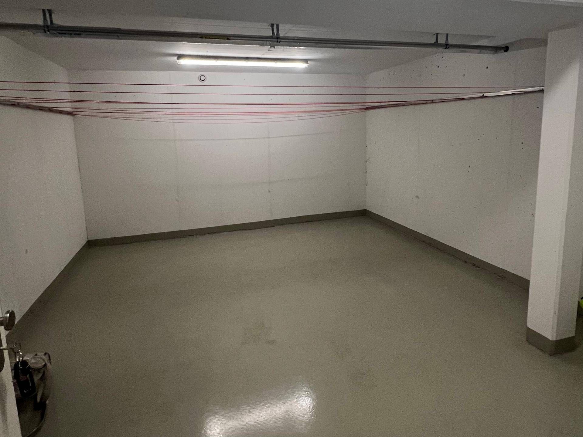 Leerer Kellerraum mit Betonboden und Wäscheleinen an der Decke.