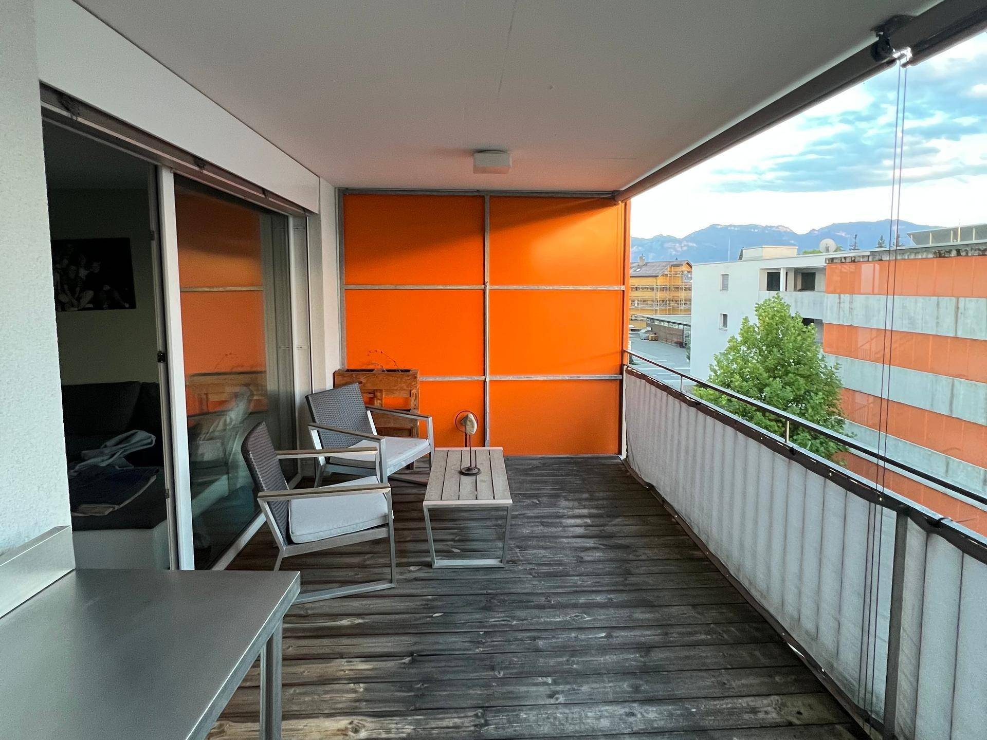 Großer Balkon mit Holzboden, modernen Möbeln und Blick auf die Stadt und Berge.