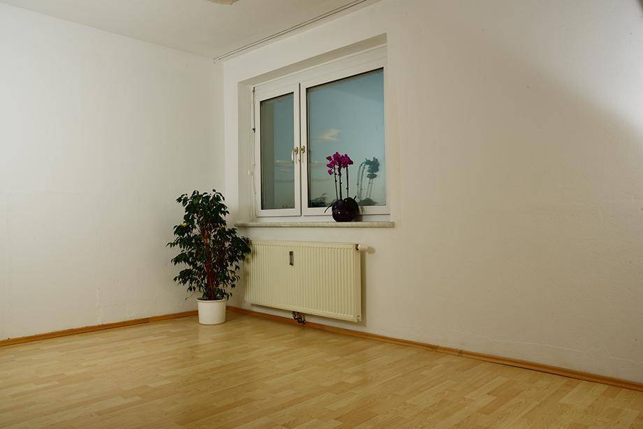 Heller Raum mit Laminatboden, weißen Wänden und einem Fenster mit Blick nach draußen.