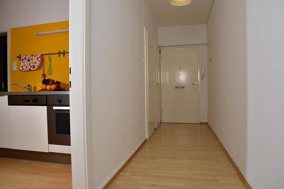 Heller Flur mit Laminatboden und weiß gestrichenen Wänden, der zum Eingangsbereich führt.