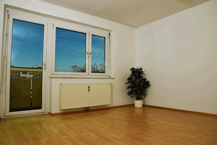 Geräumiger Raum mit Laminatboden, weißen Wänden und großen Fenstern mit Zugang zu einem französischen Balkon.