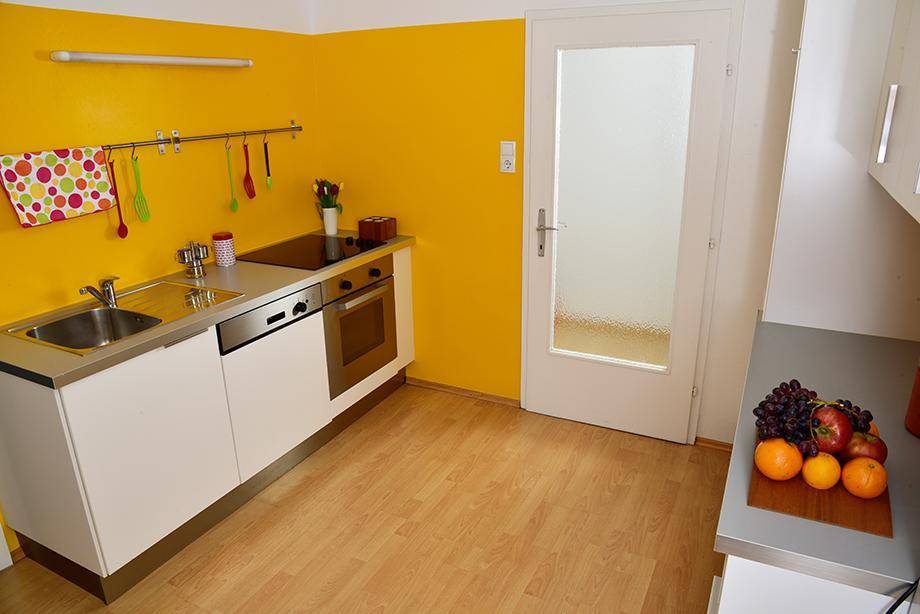 Funktionale Küchenzeile mit gelber Wand, Spüle, Kochfeld und Backofen.